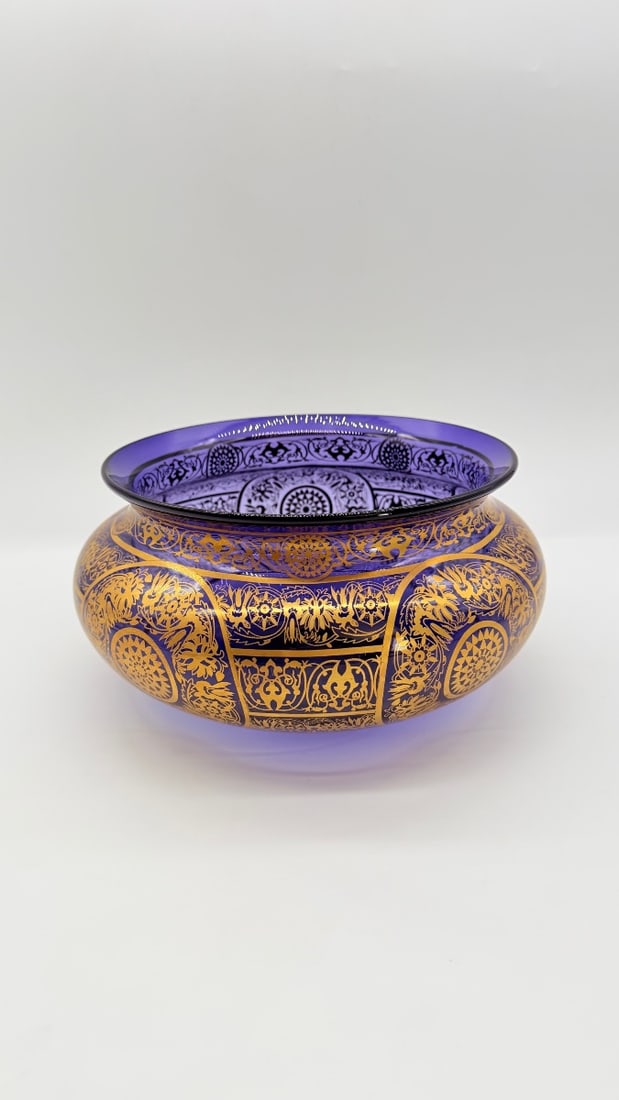 LARGE BOHEMIAN MOSER GLASS CENTERPIECE BOWL IN DARK AMETHYST WITH GILT ORIENTALIST DECORATION, LATE: A large centerpiece bowl crafted in rich, deep amethyst-tinted Bohemian glass featuring a bulbous body and flared rim. The vessel is decorated with raised gilded enamel work, intricate arabesques, flo