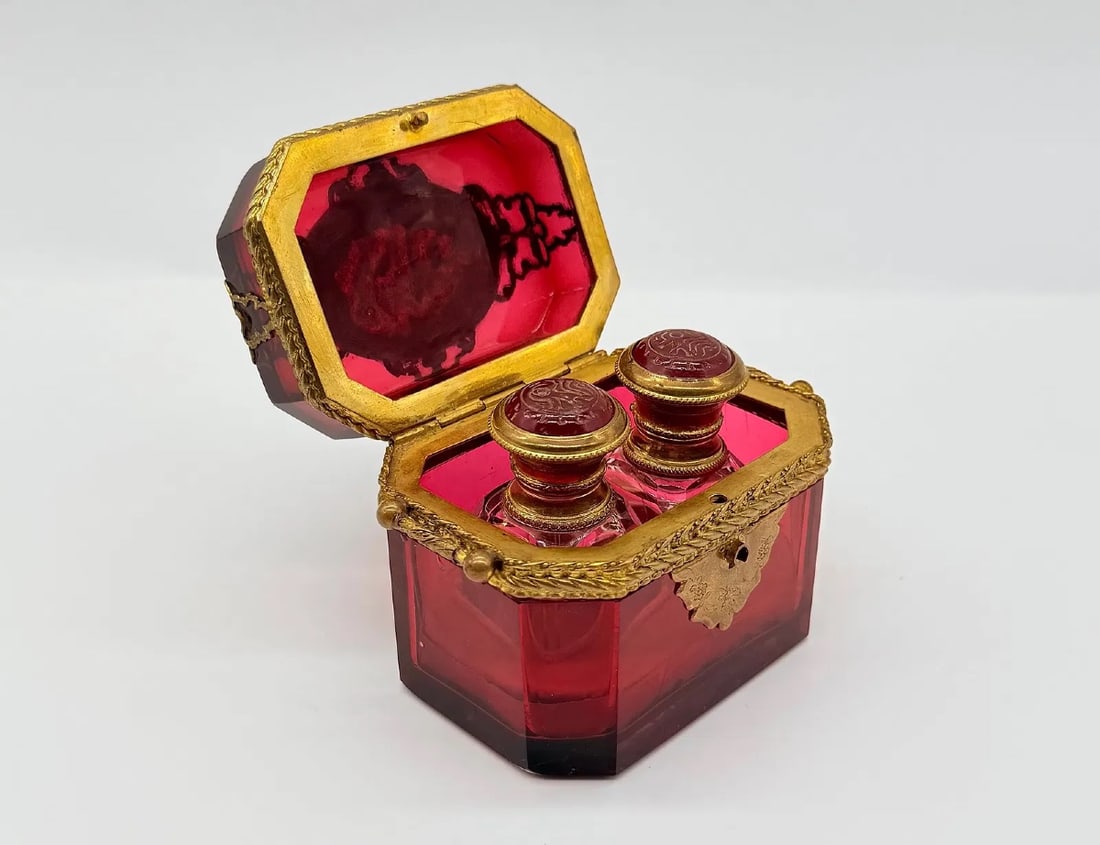BOHEMIAN RUBY GLASS PERFUME CASKET WITH PAIR OF BOTTLES, MID-19TH CENTURY: An octagonal ruby-flashed cut-glass casket featuring hinged gilt-bronze mounts with relief leaf borders and keyhole escutcheon. The interior houses a fitted pair of original matching ruby glass perfum