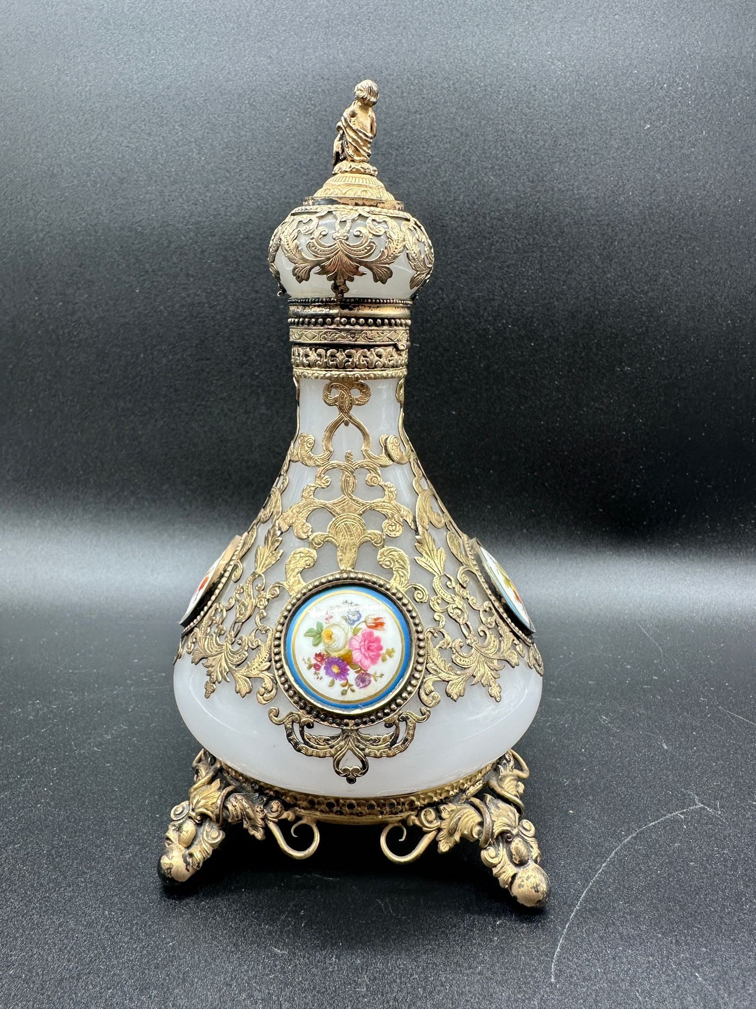 FRENCH OPALINE GLASS PERFUME BOTTLE WITH BRONZE MOUNTS AND PORCELAIN PLAQUES, 19TH CENTURY: A French 19th-century pear-shaped white opaline glass perfume bottle enclosed within openwork gilt-bronzecagework scrolling mounts. The body is inset with circular hand-painted porcelain plaques depic
