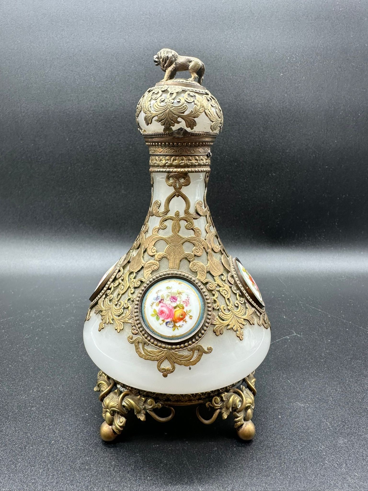 FRENCH OPALINE GLASS PERFUME BOTTLE WITH BRONZE MOUNTS AND PORCELAIN PLAQUES, 19TH CENTURY: A French 19th-century pear-shaped white opaline glass perfume bottle set within elaborate openwork gilt-bronze cagework scrolling mounts. The body features circular hand-painted porcelain plaques deco