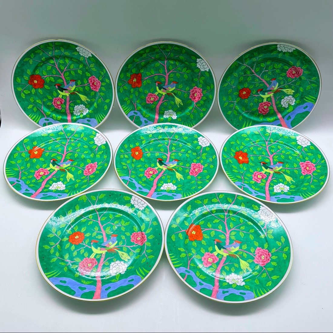 SET OF EIGHT HEREND PORCELAIN PLATES, MACAO VERDI PATTERN: A set of eight Herend porcelain plates hand-painted in the chinoiserie Macao Verdi pattern. Each plate features birds perching on pink flowering branches set against an emerald green enamel background