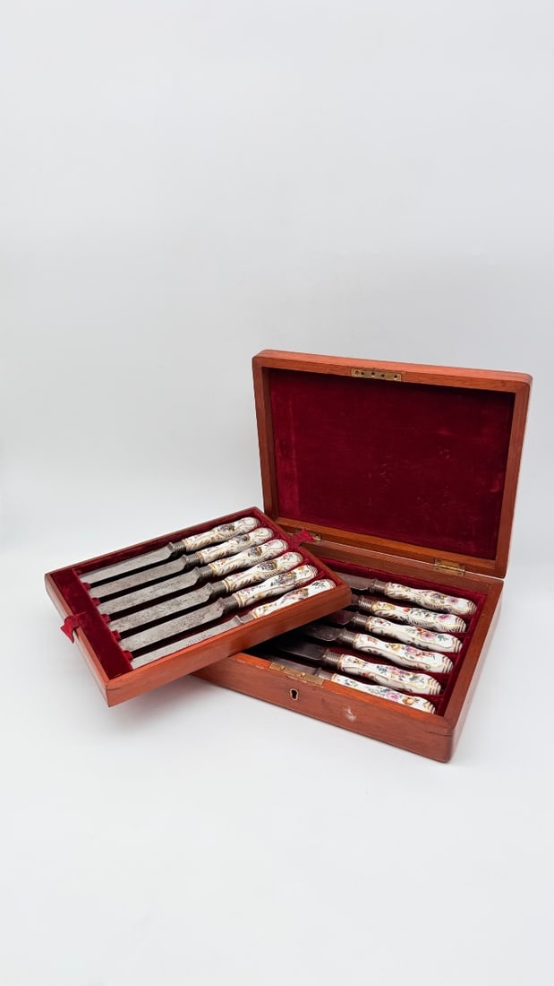 SET OF TWELVE 18TH-CENTURY MEISSEN PORCELAIN-HANDLED KNIVES IN VICTORIAN CASE: A set of twelve 18th-century porcelain-handled knives, attributed to the Meissen manufactory, featuring individual hand-painted decorations trimmed with gilt highlights. Six handles depict maritime ha