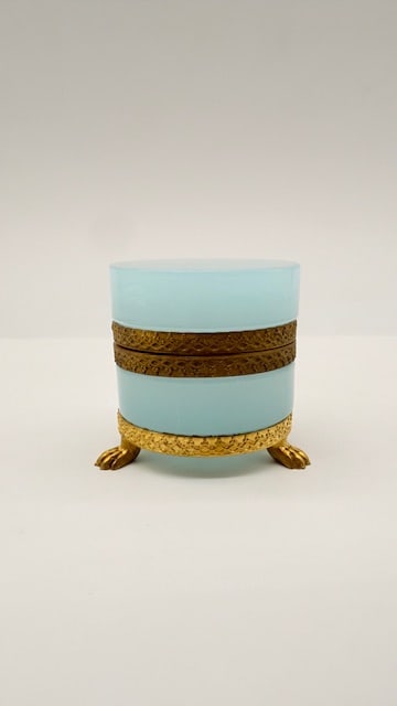 FRENCH PALE BLUE OPALINE GLASS BOX ON LION-PAW FEET: A round French pale blue opaline glass vanity or trinket box, fitted with finely chased gilded bronze mounts and a hinged collar. The box rests upon a textured circular metal ring supported by three c