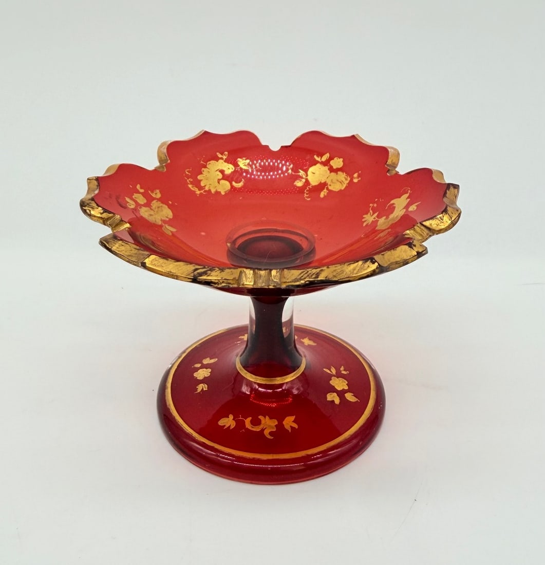 BOHEMIAN RUBY GLASS SMALL GILDED TAZZA: A small Bohemian ruby red glass footed dish (tazza), featuring a scalloped, lobed rim heavily trimmed in gold leaf. The interior bowl and domed pedestal base are hand-painted with delicate gilt floral