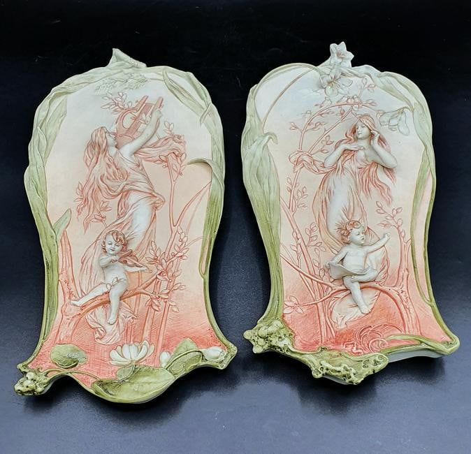 PAIR OF ART NOUVEAU BISQUE PORCELAIN BAS-RELIEF WALL PLAQUES AFTER Alphonse MUCHA (1860 ; 1939): Alphonse MUCHA (1860 ; 1939). After. A pair of unglazed bisque porcelain (biscuit) relief wall plaques depicting allegorical muses of music and song accompanied by putti nestled among floral branches.