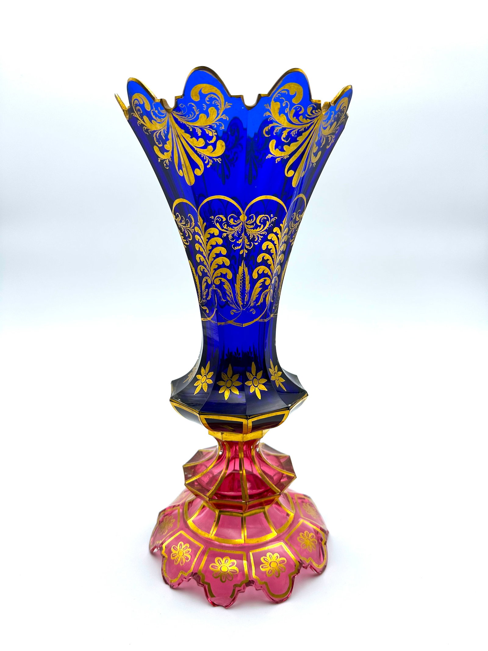 19TH-CENTURY TWO-COLOR BOHEMIAN GLASS VASE FOR THE EASTERN MARKET: Bohemian cut-glass vase featuring a flared, scalloped cobalt blue upper body raised on a multifaceted ruby-red glass pedestal and foot. The surface is embellished with gilded floral scrollwork, botani