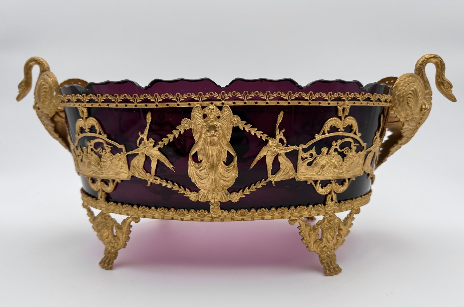 FRENCH NAPOLEON III GILT BRONZE-MOUNTED AMETHYST GLASS JARDINIÈRE: An 19th-century French centerpiece or jardinière crafted in deep dark amethyst cut glass, featuring an oval, scalloped rim. Mounted with rich gilt bronze (ormolu) openwork applique depicting winged v