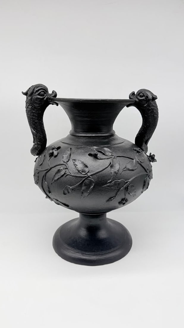 Italian Grand Tour Black-glazed Terracotta Urn With Dolphin Handles, 19th Century: Two?handled urn?vase with dolphin handles in black?glazed terracotta, the swollen body decorated with raised leafy laurel branches, with flared neck and pedestal foot on circular base.Italy, Grand Tou