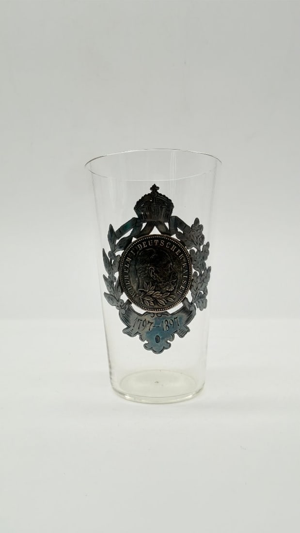 Commemorative Glass Beaker With Wilhelm I Medallion, Germany, 1897: A commemorative truncated-conical glass goblet, the front adorned with a raised silver-plated metal plaque depicting the profile of Emperor Wilhelm I in a medallion surrounded by a laurel and oak wrea