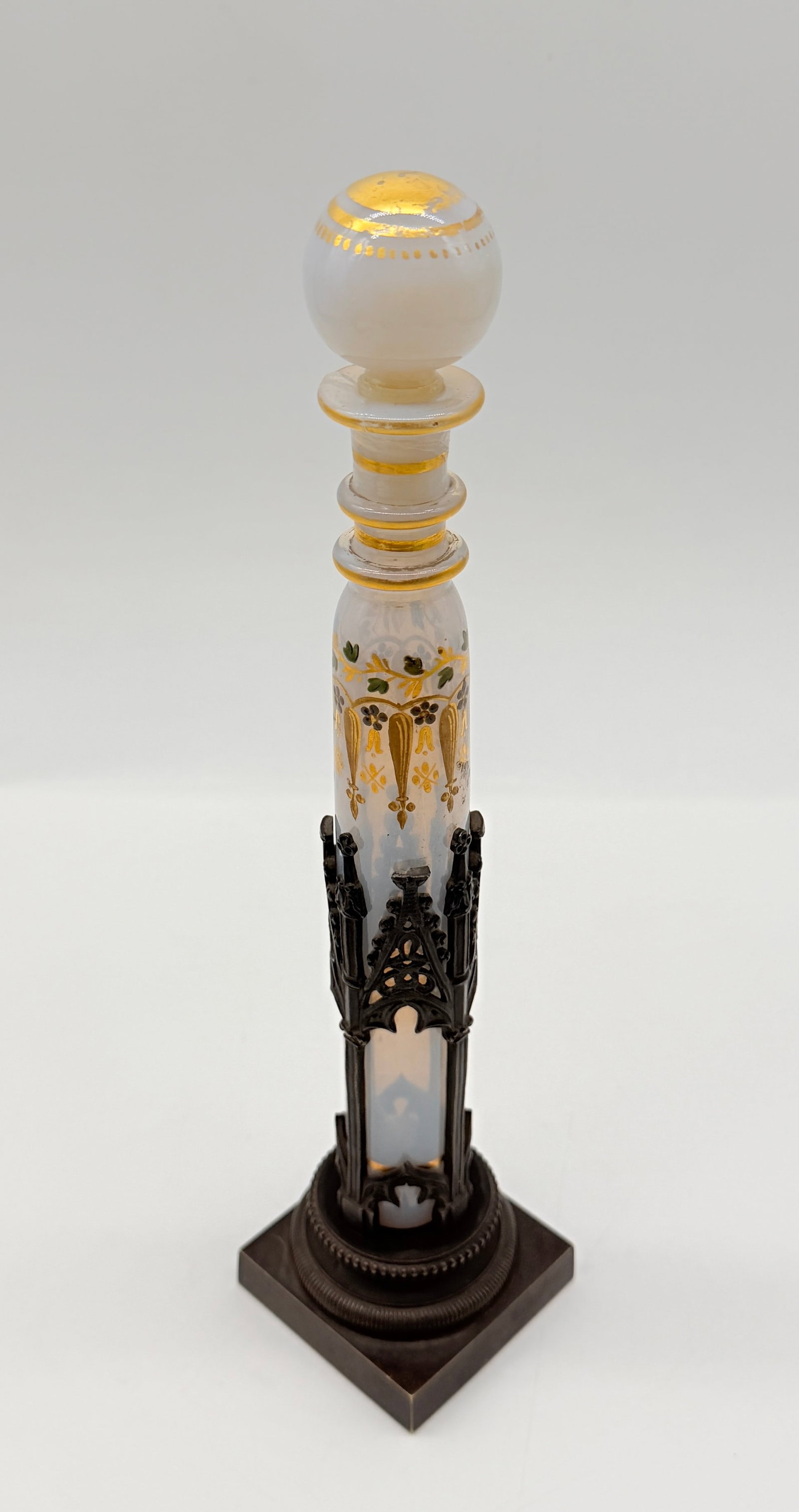 19TH-CENTURY OPALINE GLASS SCENT BOTTLE IN GOTHIC REVIVAL HOLDER: Scent bottle in translucent white opaline glass, finely hand-painted with gilded Gothic arches and floral vines. Accompanied by its original dark patinated metal holder designed in the Gothic Revival 