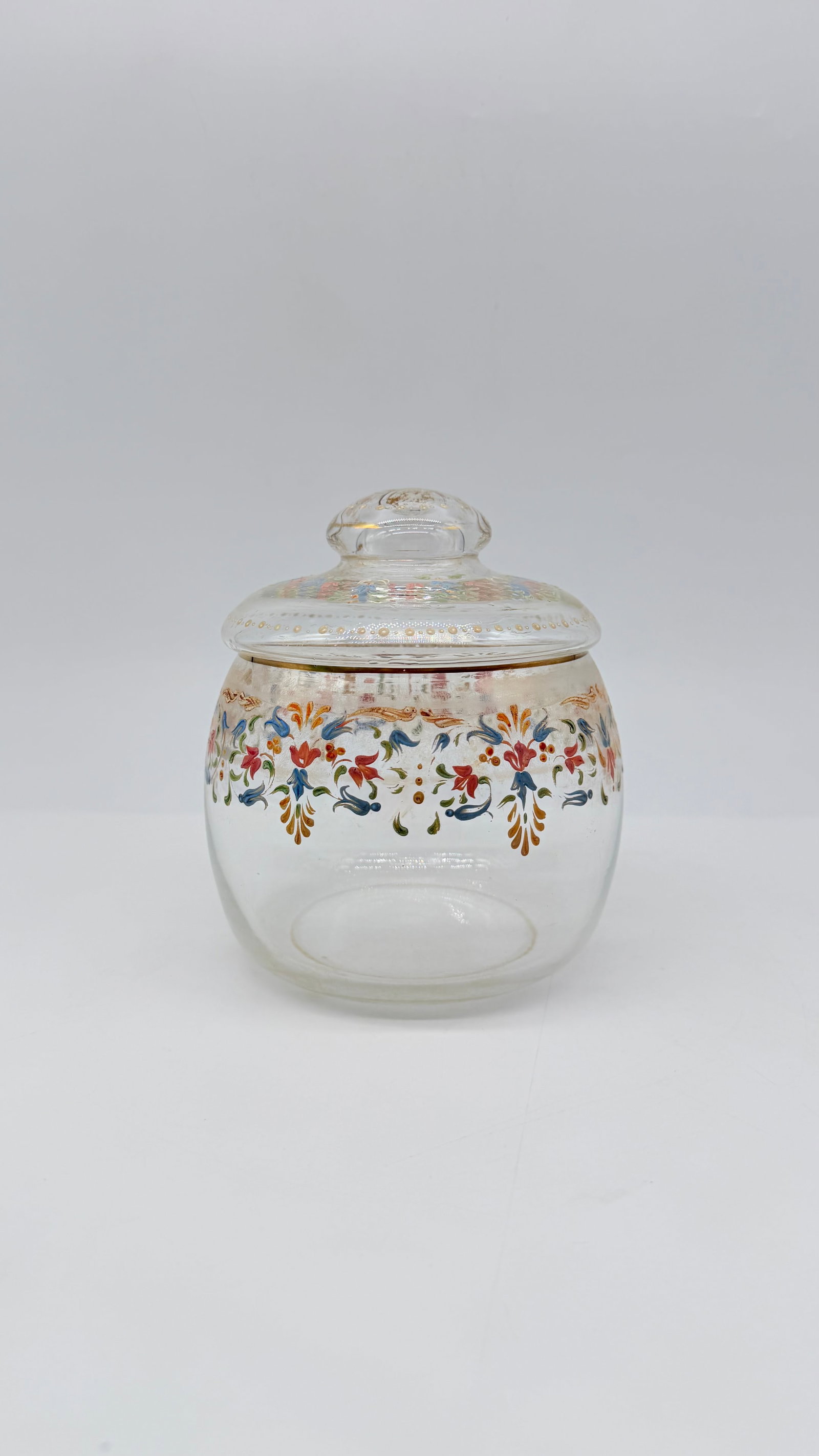 19TH-CENTURY ENAMELLED AND GILDED GLASS COVERED JAR: Clear glass covered jar or candy dish (bonbonnière), finely hand-painted in polychrome enamel with scrolling floral Arabesque patterns in blue, red, and green, accented with gilded borders. Complete 
