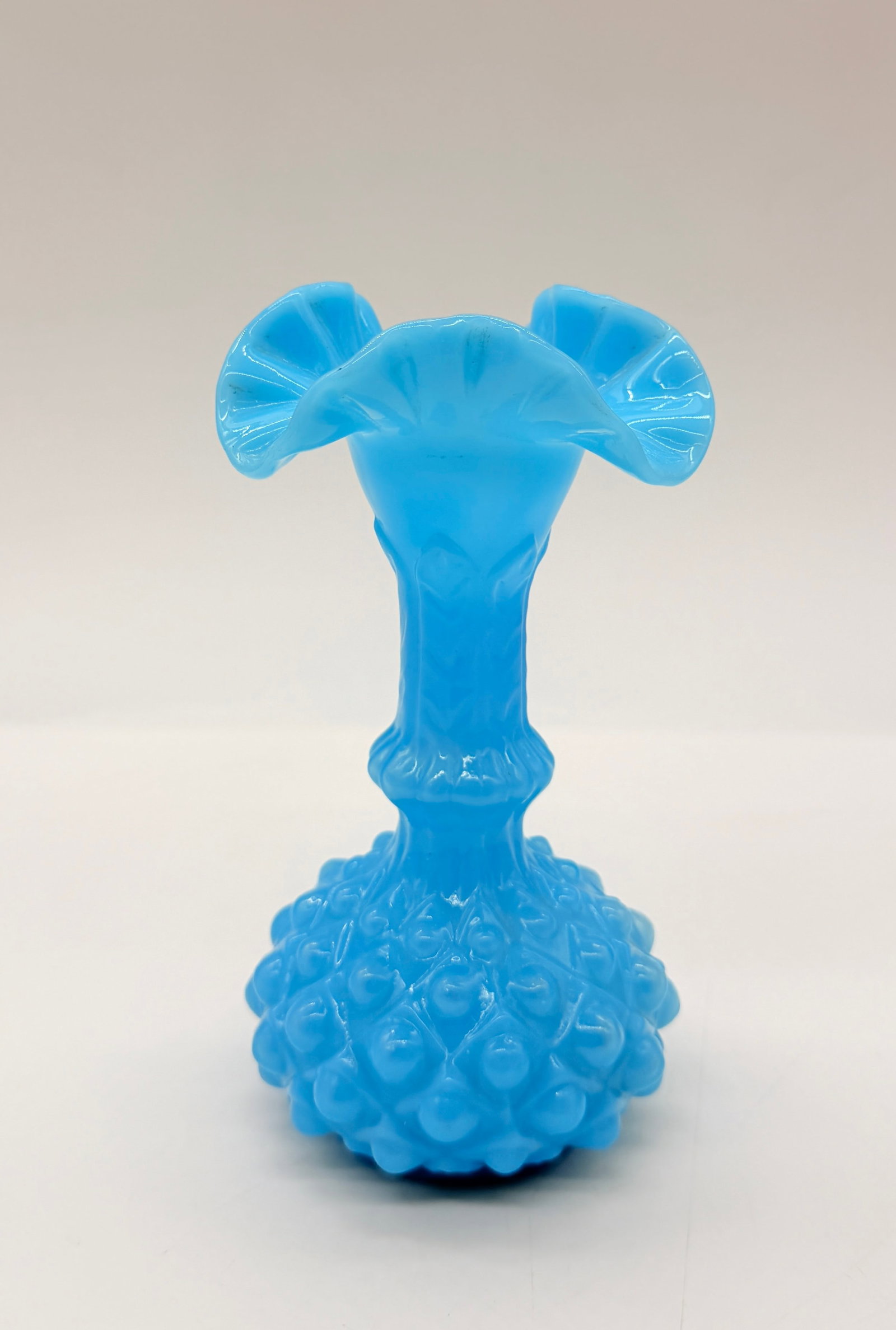 FRENCH OPALESCENT / MILK GLASS HOBNAIL VASE #2: A bright turquoise blue opaque glass vase featuring a flared, crimped rim, a molded neck with leaf motifs, and a bulbous base decorated with a raised hobnail pattern.FRANCE. Mid-20th century (c. 1950s