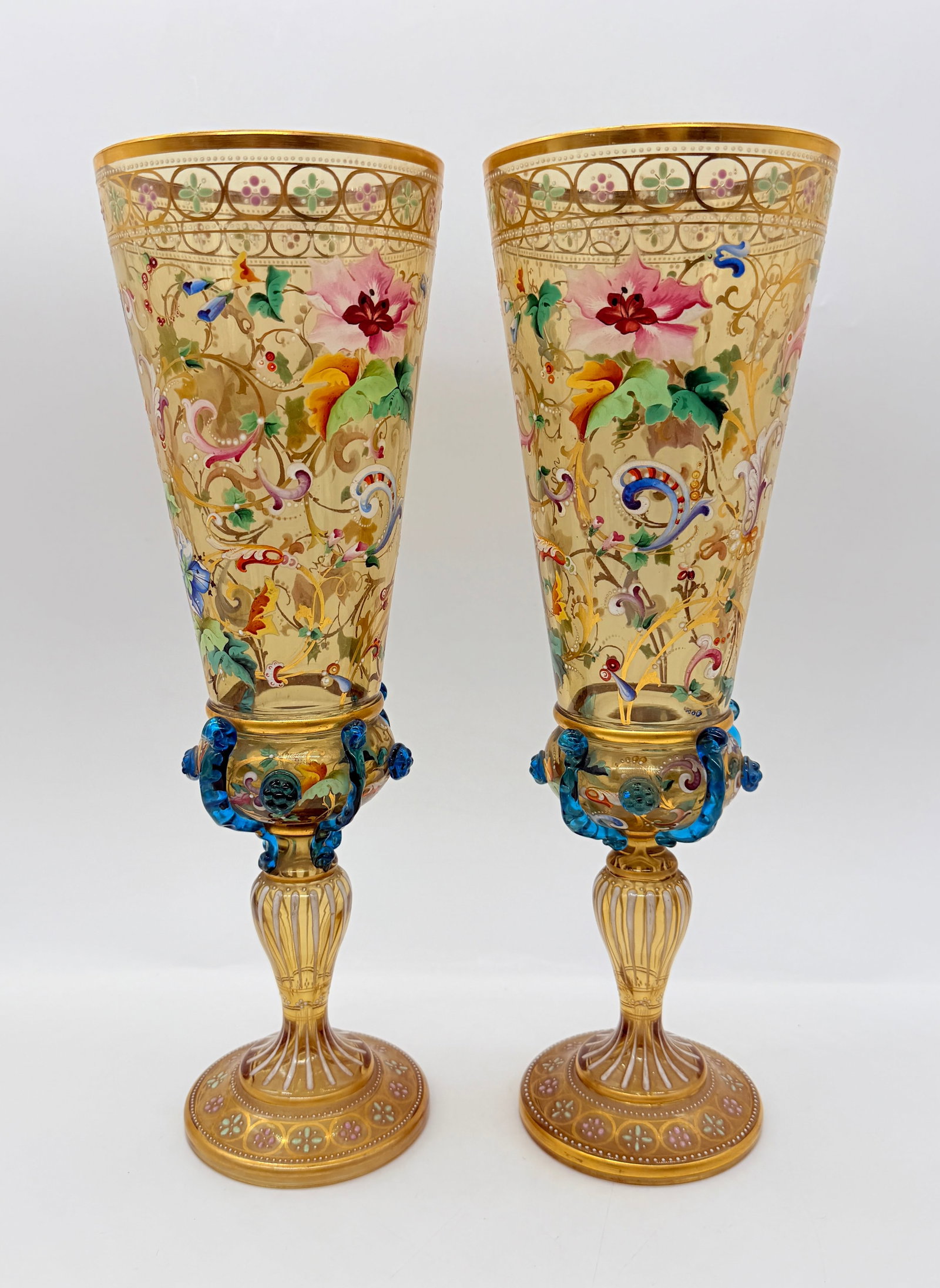 PAIR OF 19TH-CENTURY LOBMEYR ENAMELED GLASS VASES / GOBLETS: A pair of amber-tinted clear glass chalice-form vases featuring flared trumpet rims, blue applied scrolled handles around the central knop, and pedestal bases. Finely decorated with polychrome hand-pa
