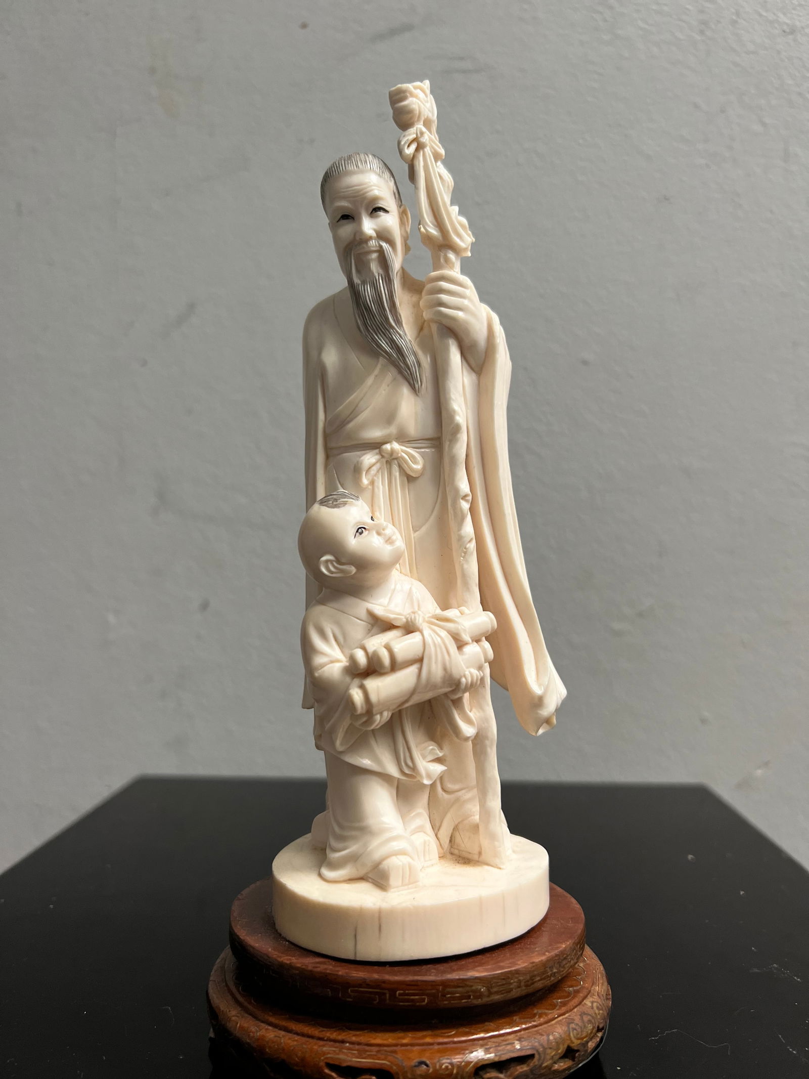 Stunning Early 20C Chinese Hand Carved Sage on a Wood Base: This exquisite piece is a stunning example of early 20th century Chinese artistry. The intricately carved bone figurine of a sage sits atop a wooden base, measuring 9 inches in height. The ivory color