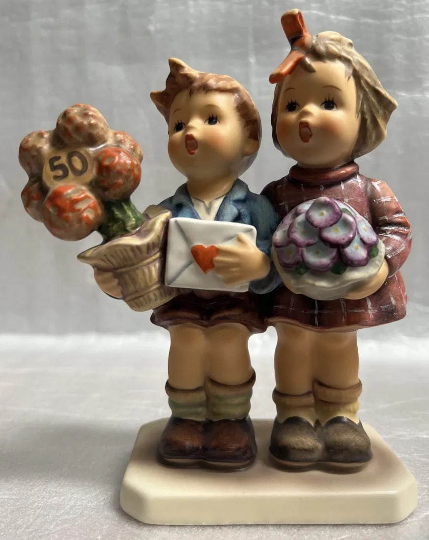 GOEBEL FIGURINE, LOVE LIVES ON 50TH ANNIVERSARY 6" TALL 5" WIDE: GOEBEL FIGURINE, LOVE LIVES ON 50TH ANNIVERSARY 6" TALL 5" WIDE Each figurine is beautifully crafted with intricate details and made from high-quality porcelain. The collection is part of the Hummel s