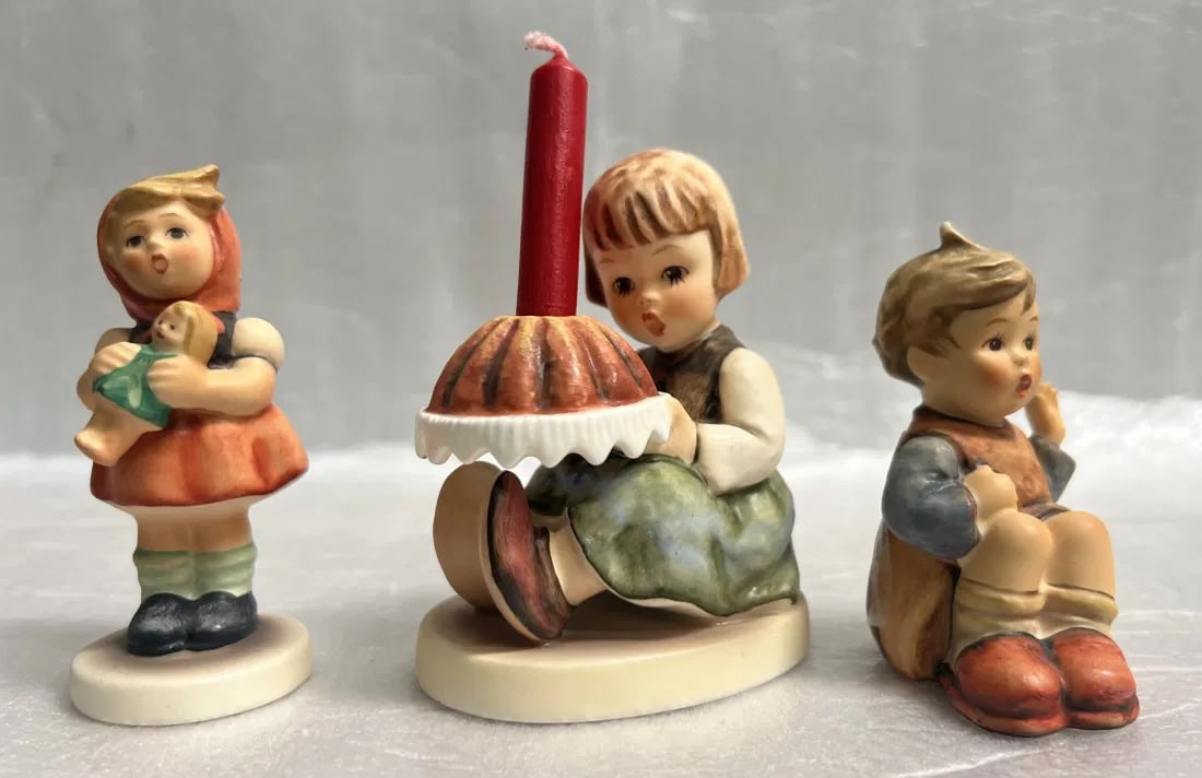 LOT OF THREE GOEBEL FIGURINE, "BIRTHDAY CANDLE""HELLO IM HERE" & "GIRL W DOLL": This lot of three Goebel figurines includes "Birthday Candle," "Hello I'm Here," and "Girl With a Doll." Each figurine is beautifully crafted with intricate details and made from high-quality porcelai