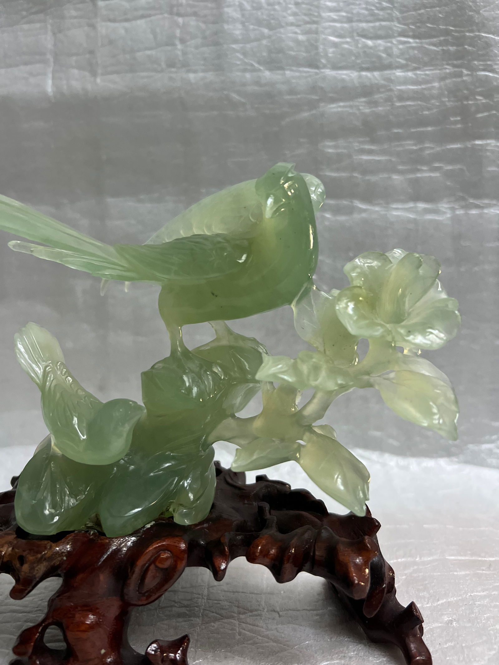 Chinese Light Green Jade Carving Featuring Birds and Flowers on a Wood Base: This Chinese light green jade carving features intricate bird and flower designs on a wood base. The abstract sculpture, dating back to the late 20th century, showcases traditional Chinese craftsmansh