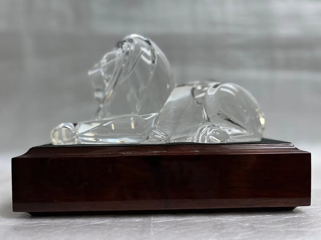 Steuben Crystal Lion Sculpture Designed by Lloyd Atkins in 1996 on a Wooden Base: The Steuben Crystal Lion Sculpture, designed by Lloyd Atkins in 1996 on a wooden base, is a large and intricately detailed piece of art. Crafted from crystal, this sculpture depicts a lion in a striki