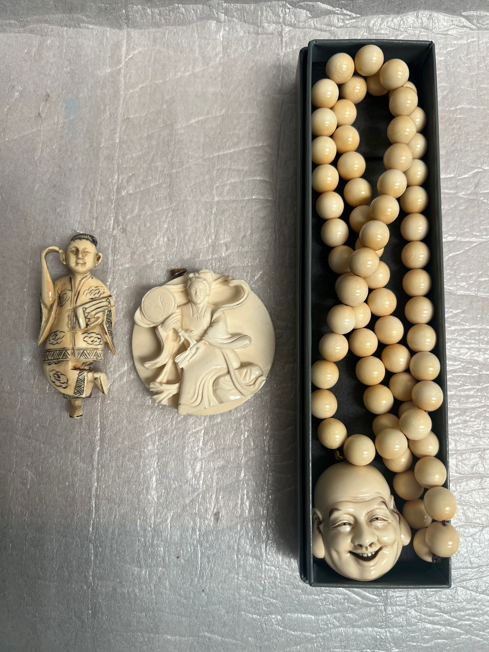 A Collection of Hand Carved Pendents and Budda Necklace: three hand-carved pieces, likely made of bone or a similar material, with an East Asian aesthetic, possibly Japanese or Chinese based on the figures depicted. Beaded Necklace with Carved Head Pendant:
