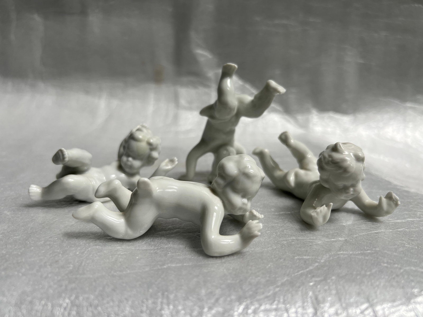 Set of 4 White Porcelain Cherubs at Play: Set of Vintage Porcelain Putti/Cherub FigurinesCharming Collectibles: Delightful white porcelain figurines depicting playful cherubs or putti in various poses.Material: Fine quality porcelain with a s