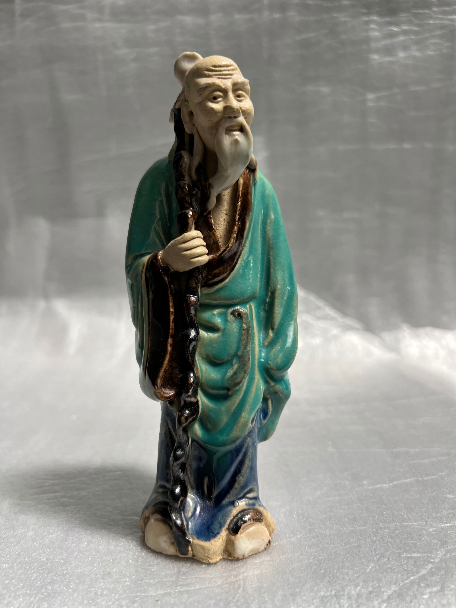 Shiwan Mudman Figurine A Traditional Clay Pottery Art: Description of the Statue:Subject: The figurine depicts an old man, likely a wise figure or a fisherman, characterized by his unglazed face and hands, which show fine details like wrinkles. He has a p
