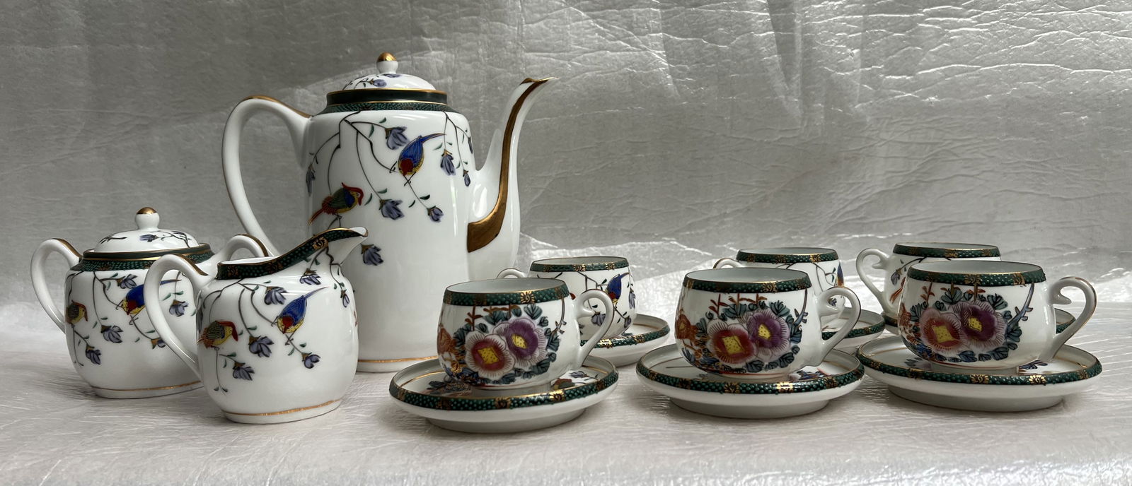 Zsolnay Hungary porcelain tea set: Zsolnay Hungary porcelain tea set, specifically from the "Four Seasons Color" collection, which features a vibrant bird and flower pattern. The set includes a teapot, creamer, sugar bowl, and several
