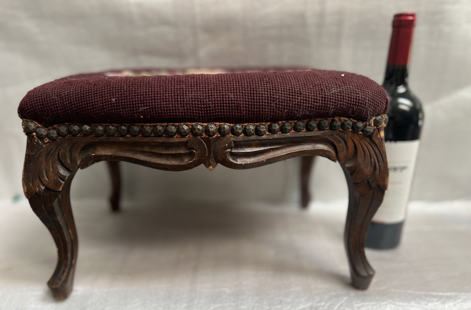 A Vintage Needlepoint Footstall with Maroon Floral Tapestry: This is a vintage needlepoint footstool with a maroon floral tapestry top, dark carved wooden cabriole legs, and nailhead trim. 15 x 11 x 9