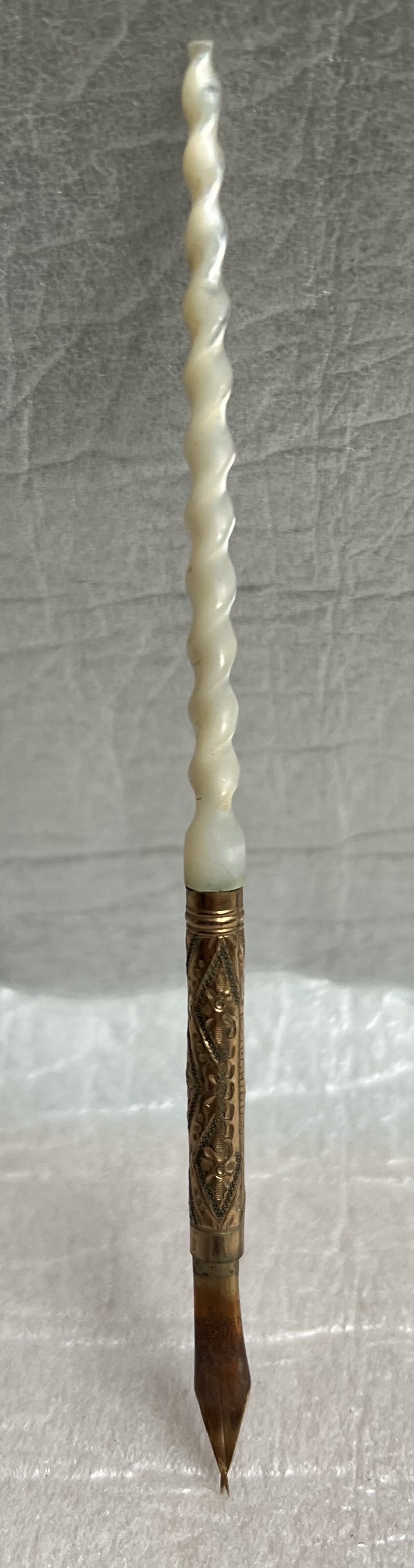 Vintage Dip Pen with Mother of Pearl Handle: The object in the image is a vintage dip pen with an ornate handle. Dip pens are writing instruments that have no ink reservoir and must be repeatedly dipped into an inkwell for ink. The handle appear