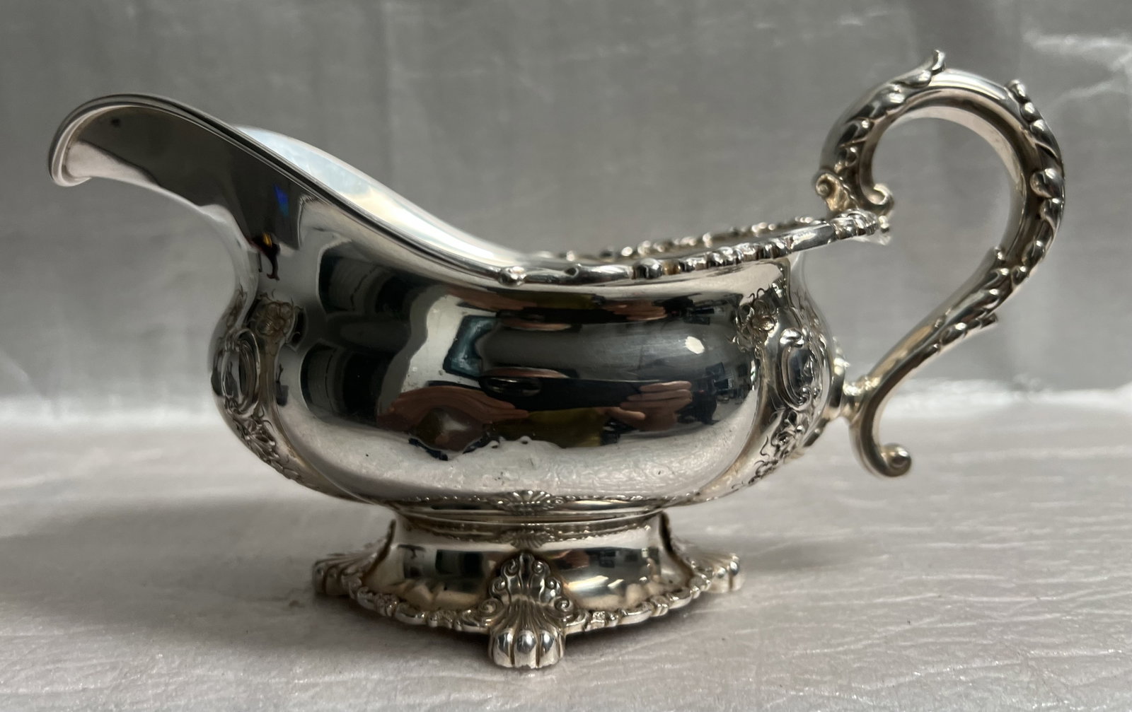 Tiffany & Co Victorian Silver Gravey or Sauce Boat: The item pictured is an ornate, Victorian-style silver gravy or sauce boat. It is a footed piece with a handle and spout, featuring extensive repoussé and chase work, which includes floral, scroll, a