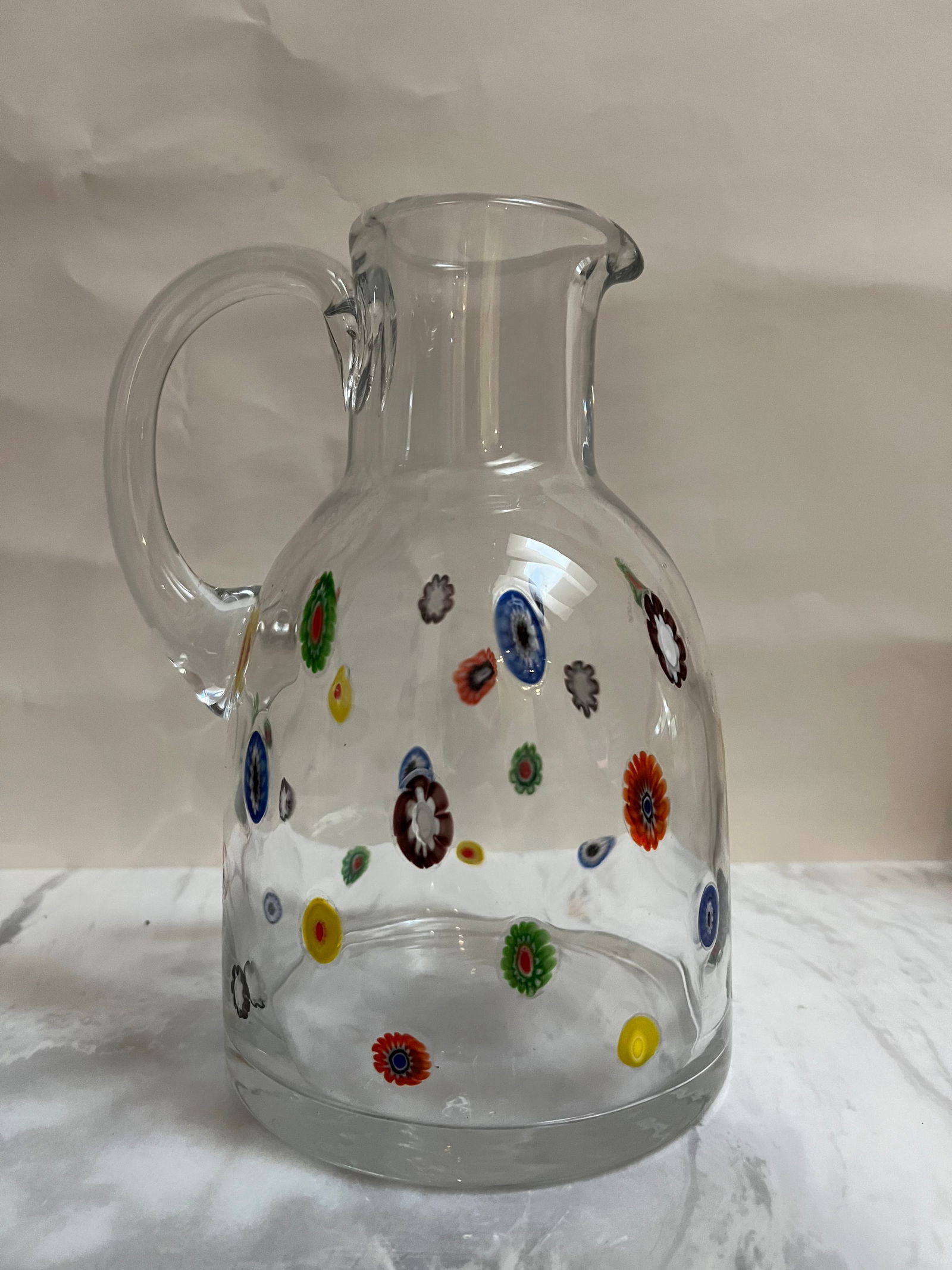 Large Hand-Blown Millefiori Glass Cruet / Pitcher - 9.5" Italian Style Decorative Glass: Style: Authentic Murano-style art glass with a classic "Millefiori" floral pattern.• Design: The pitcher is crafted from clear, hand-blown glass with colorful, mosaic-like floral "murrine" (canes