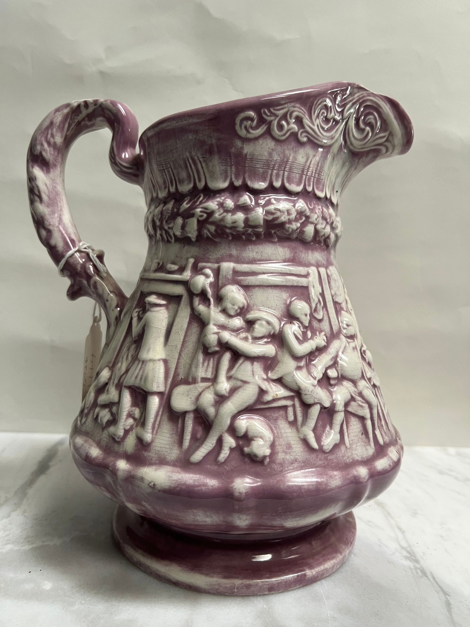 Antique 19th Century "Tam O' Shanter" Relief-Molded Mulberry/Purple Pitcher - 9": This pitcher is an antique Tam O' Shanter relief-molded jug, most likely made by Ridgway or a similar Staffordshire pottery in England during the mid-to-late 19th century. The design is based on the f