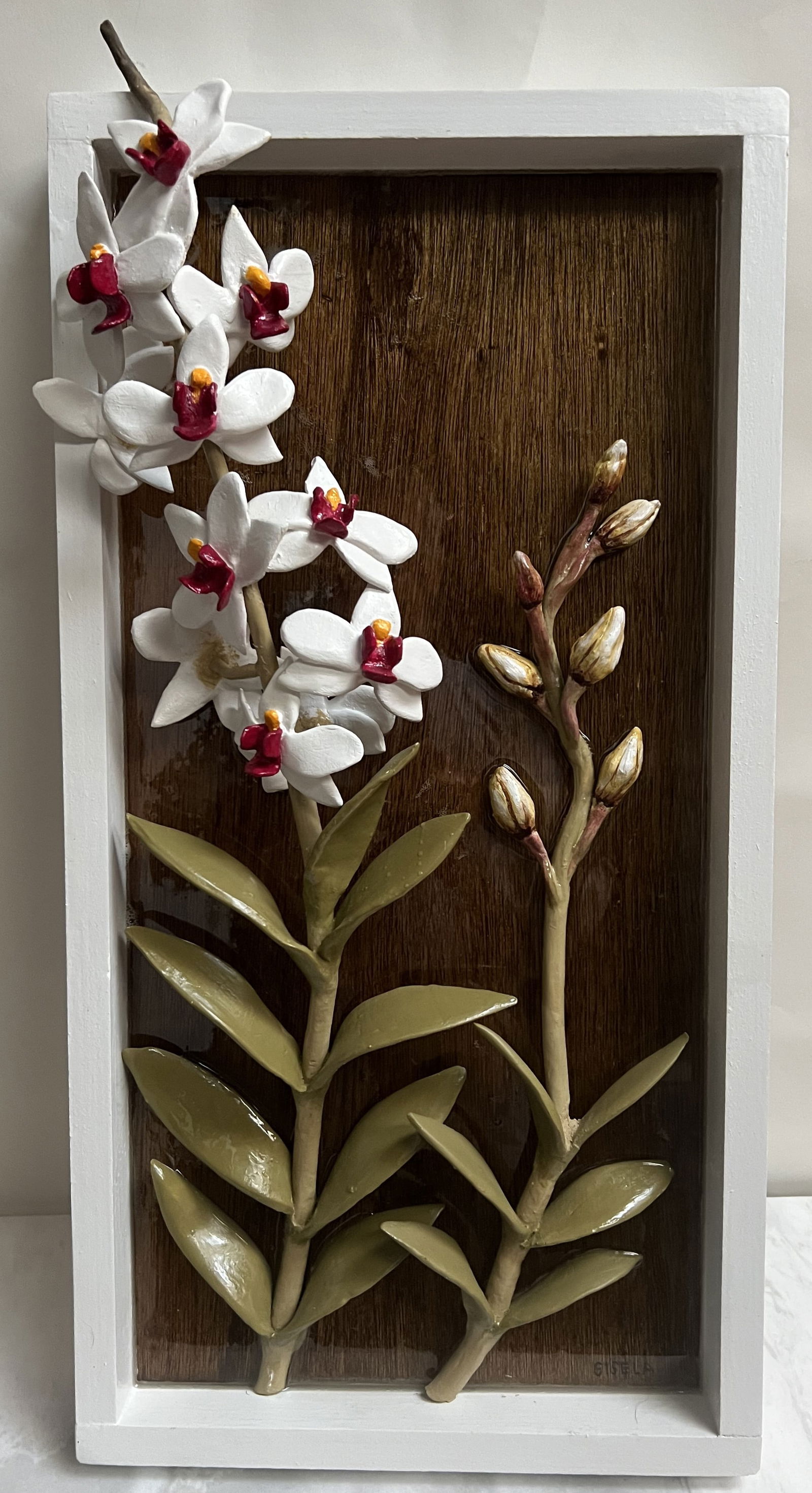 Gisela Pferdekamper Original 3D Ceramic Orchid Relief - 12x24 Signed Wood Panel: Artistic Description• Subject: A high-relief sculptural depiction of three White Orchids with vibrant yellow and pink centers.• Medium: Hand-formed ceramic elements mounted onto a rich, vert