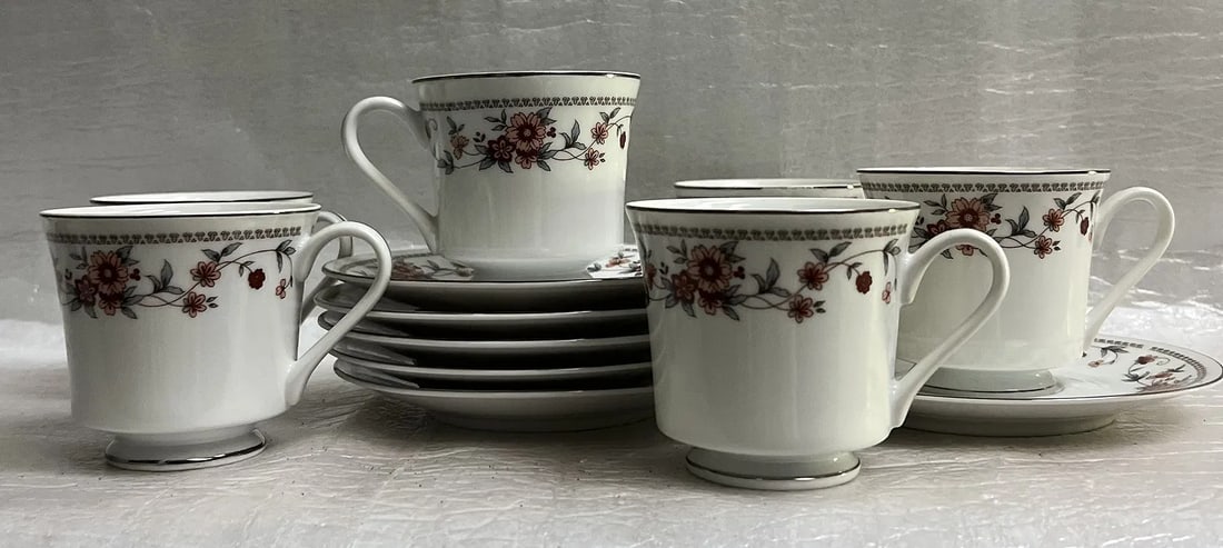 Set of 12 Pieces Sheffield Anniversary Porcelain Fine China 6 Cups and Saucers: This is a piece of Sheffield Anniversary Porcelain Fine China, set of 6 cups and saucers, characterized by its floral pattern with peach/pink and rust-colored flowers, gray/blue leaves, and a silver r