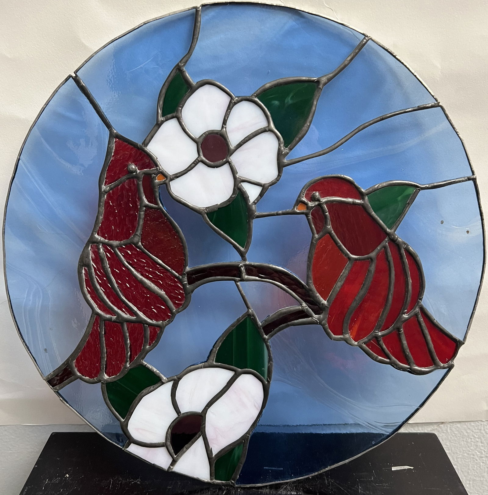 Cardinals in Bloom: 12-Inch Roundel Suncatcher: This 12-inch circular stained glass panel features a classic nature motif of two vibrant Northern Cardinals perched on a branch among white Dogwood flowers.• Design: The composition uses a mix of