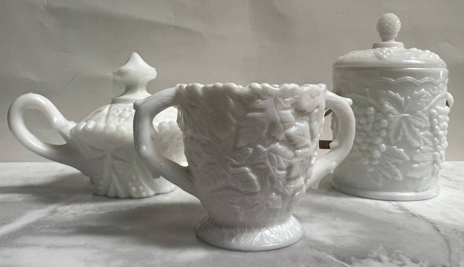 Vintage Milk Glass 3-Piece Set: Grape & Leaf Biscuit Jar, Creamer, and Footed Sugar Bowl: This beautiful 3-piece set is a classic example of Mid-Century Milk Glass, featuring two of the most popular patterns from that era: the "Harvest Grape" and the "Daisy & Button" (or Star) styles.Based