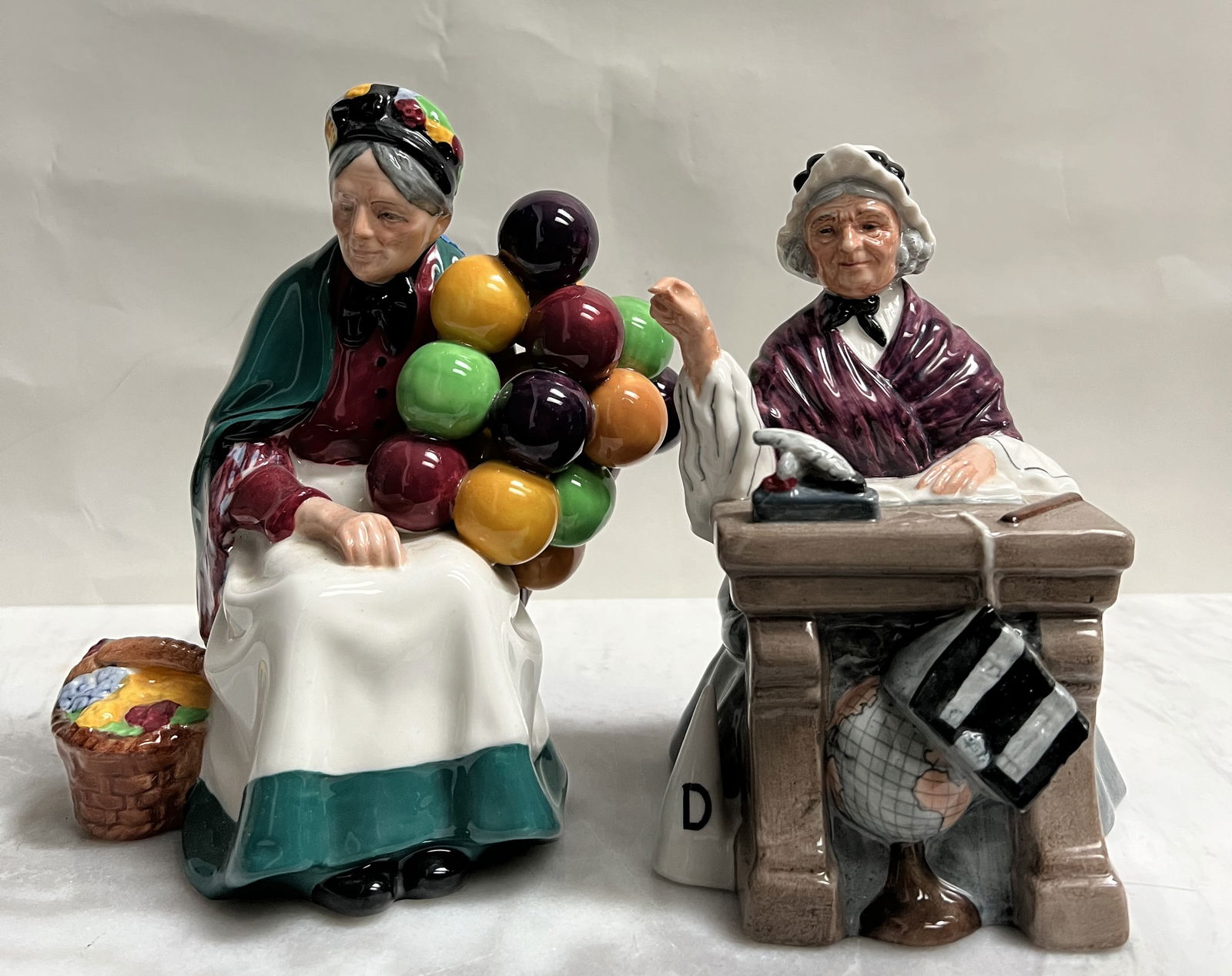 Vintage Royal Doulton Figurines Set - "The Old Balloon Seller" HN 1315 & "Schoolmarm" HN 2223: These two figurines are classic, highly collectible pieces from Royal Doulton, a renowned British ceramic manufacturer. Both figurines are marked with the official Royal Doulton seal on the base.&bull
