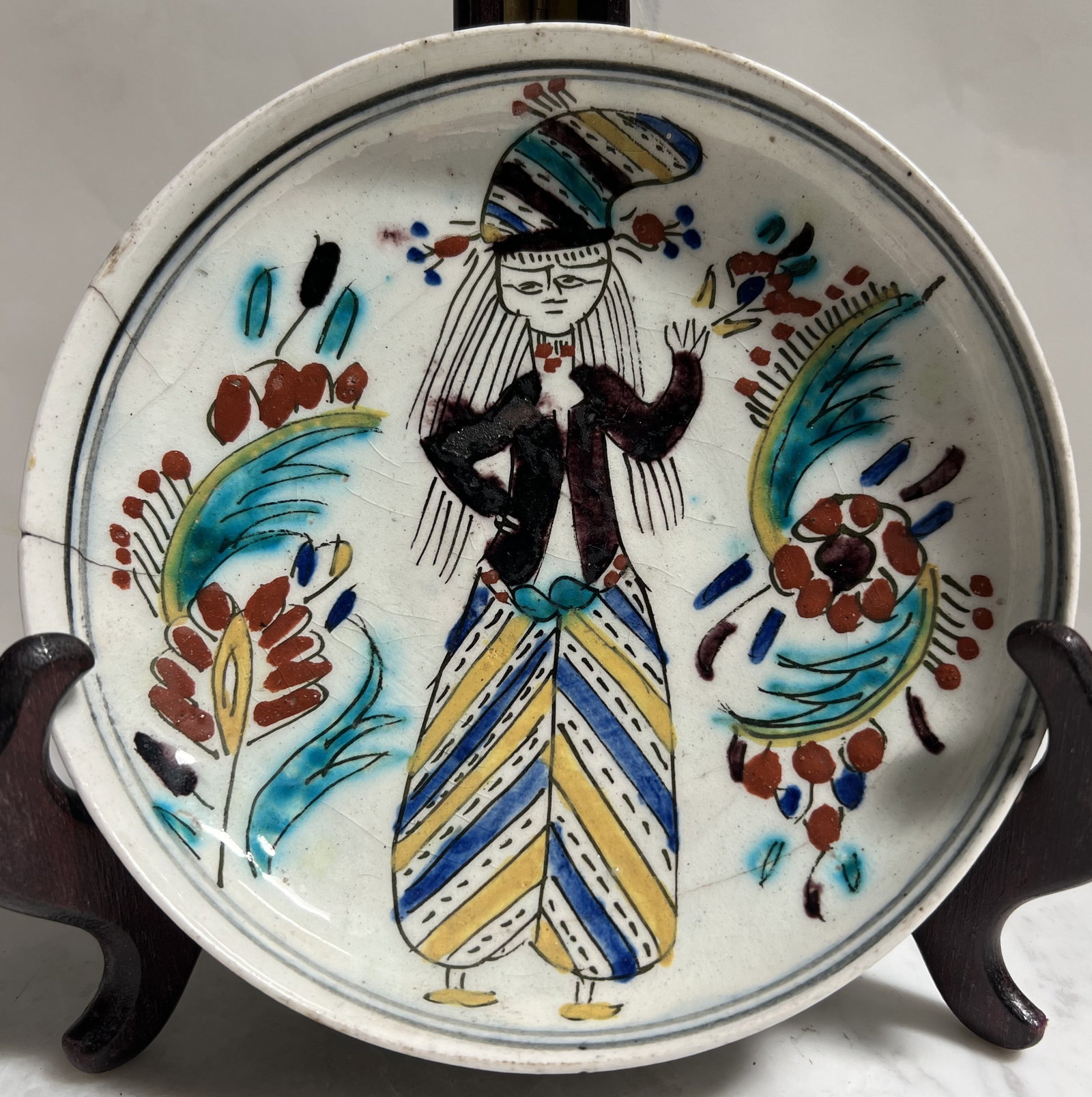 Antique Turkish Plate: • Origin: Kutahya, Turkey. • Period: Early 20th Century (Late Ottoman/Early Republic era). • Subject: A charming hand-painted depiction of a woman wearing a striped alvar (traditional t