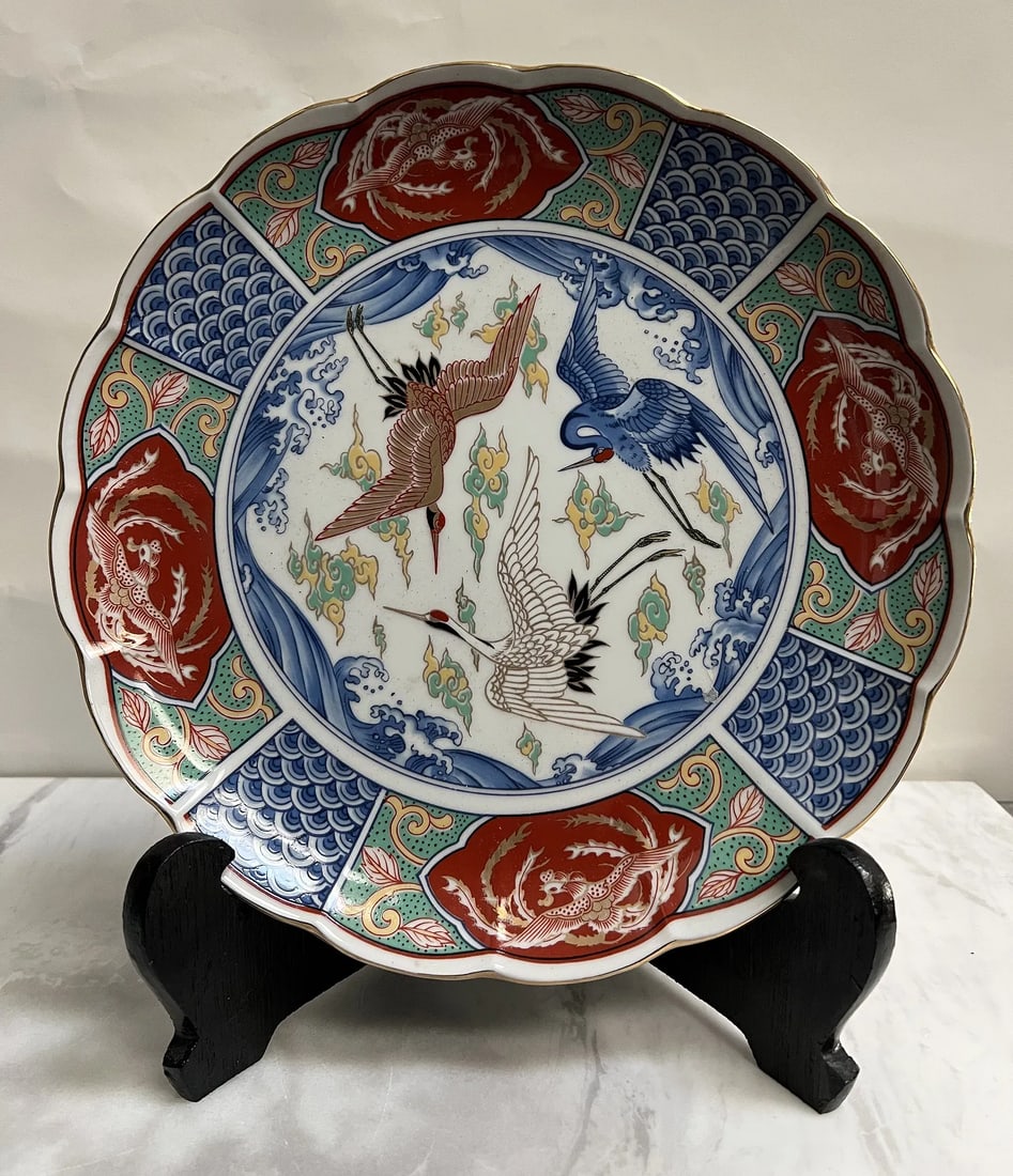 Vintage Japanese Imari Porcelain Charger – Hand-Painted Flying Cranes & Phoenix Motif, Scalloped: Product Description• Origin: Made in Japan (Features original red and gold "Made in Japan" foil sticker and blue underglaze character mark on the base).• Design: The central medallion depict