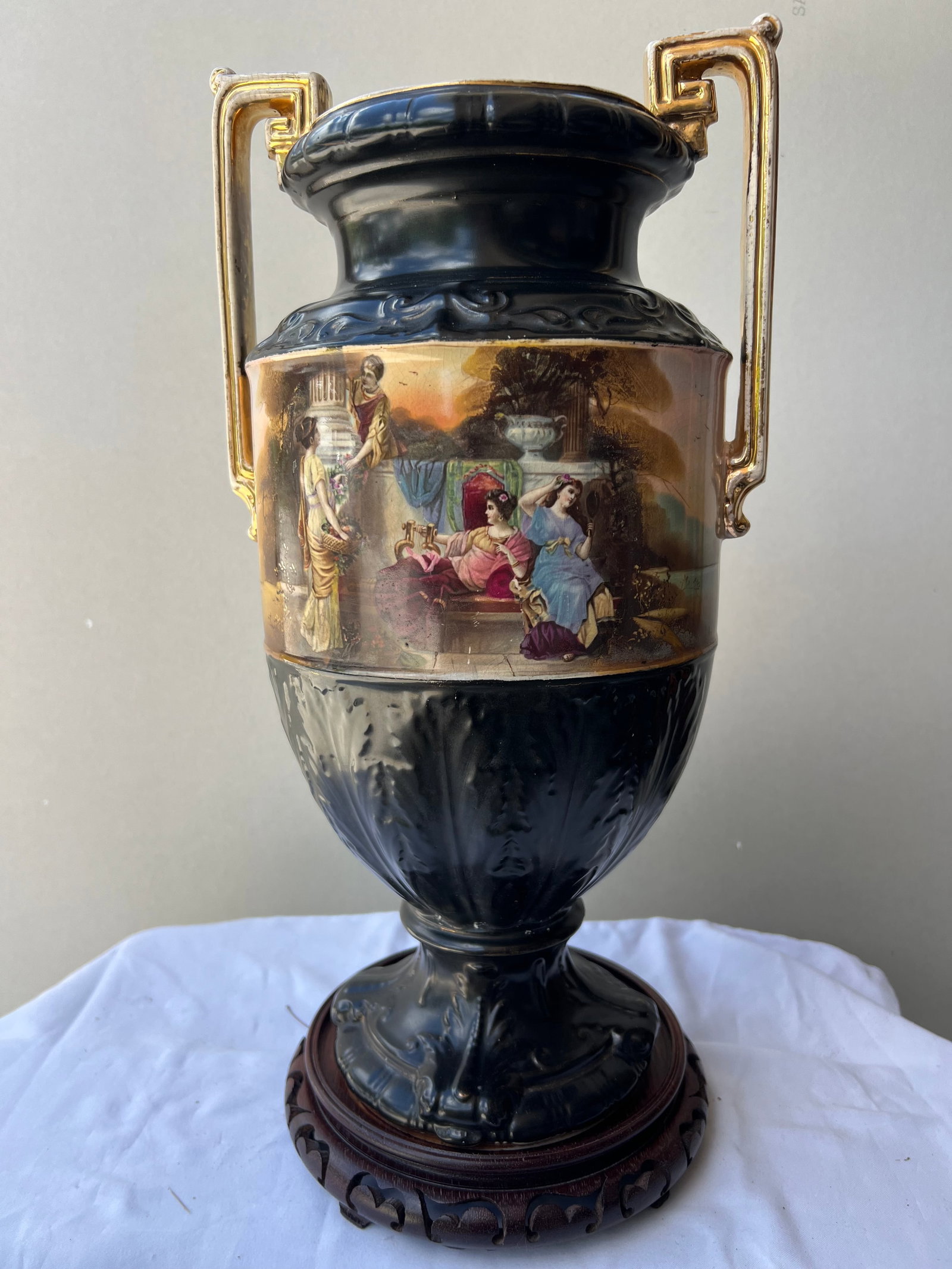 Early 20th Century Amphora Style Classical Earthenware Vase on Wood Stand: Form & Style: This is a large neoclassical-style earthenware or semi-porcelain amphora vase featuring dual geometric, Greek-key handles with gilded highlights . The body features a molded, relief-deco