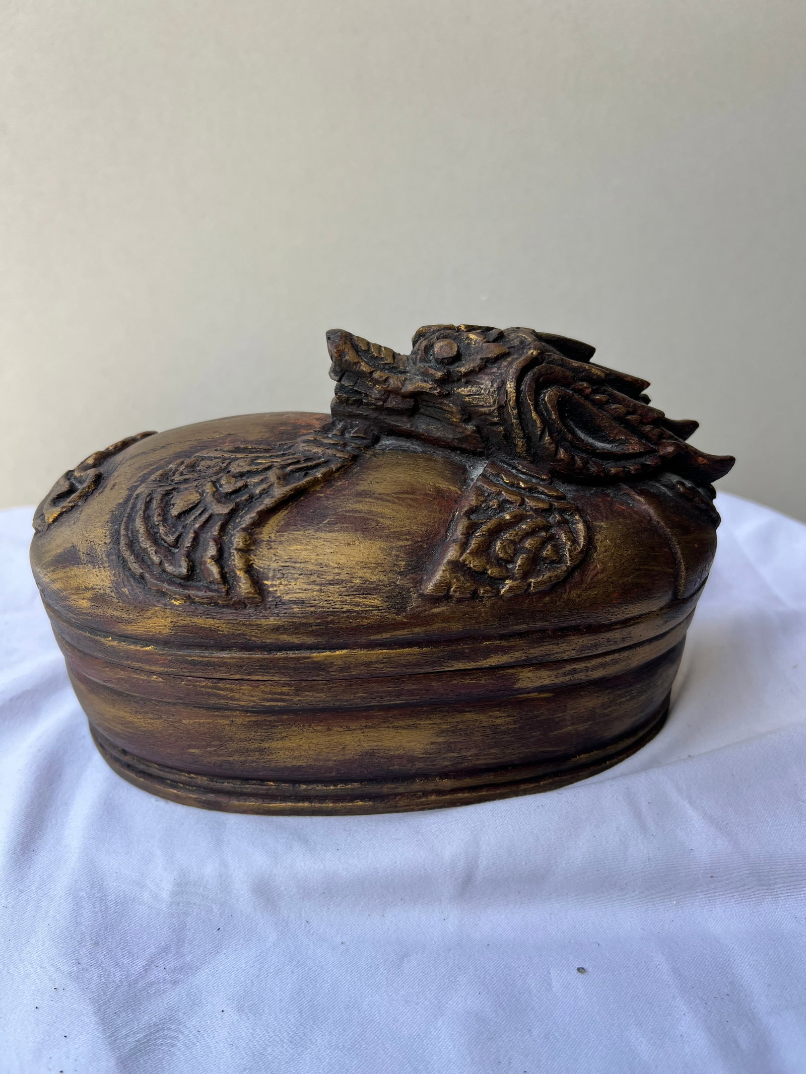 Carved Wooden Mythological Creature Trinket Box: this is an elongated, peanut- or kidney-shaped wooden trinket box. The removable lid is carved with a low-relief mythical creature, featuring a stylized draconic head positioned at one end and low-rel