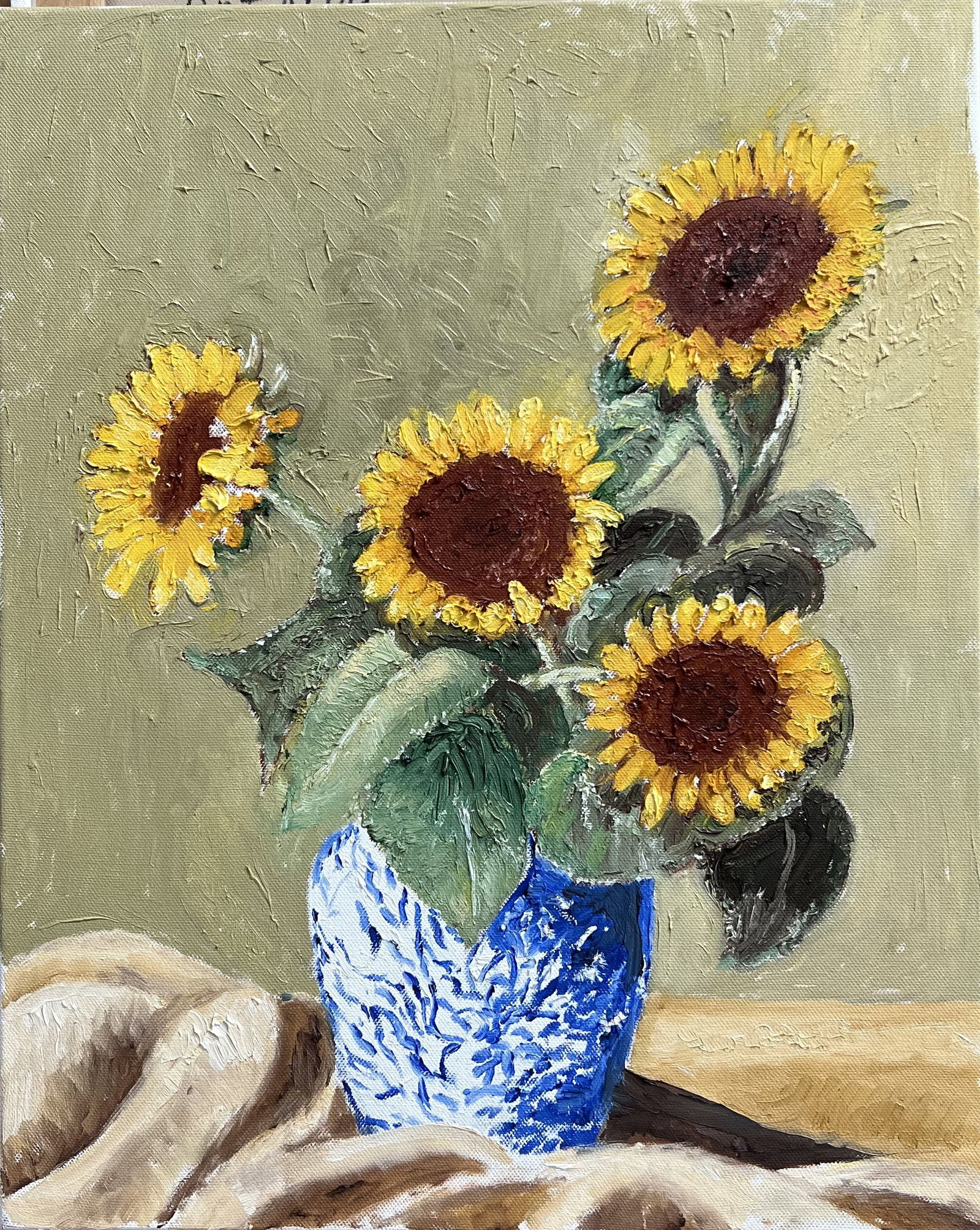 Art Krug Original Oil Painting Sunflowers in Blue Ceramic Vase Still Life 20x16: This vibrant original still-life oil on canvas features a bouquet of bright yellow sunflowers arranged in a blue and white patterned ceramic vase draped against a draped neutral cloth backdrop. Execut