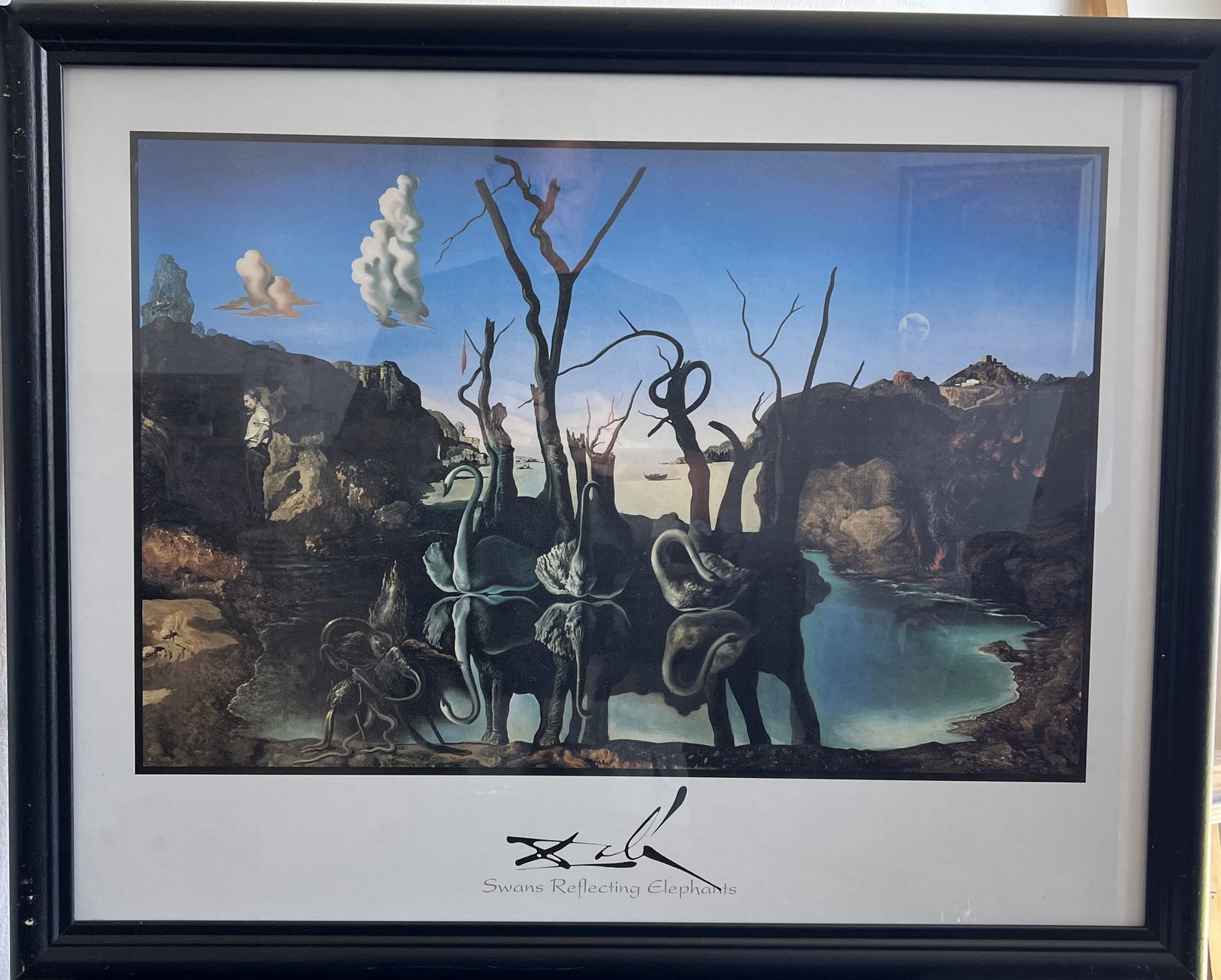 Salvador Dali "Swans Reflecting Elephants" Framed Vintage Fine Art Print 30" x 25": This framed print features Salvador Dalí’s famous 1937 Surrealist masterpiece, Swans Reflecting Elephants. The artwork depicts three swans on a tranquil lake backed by bare trees; their reflections