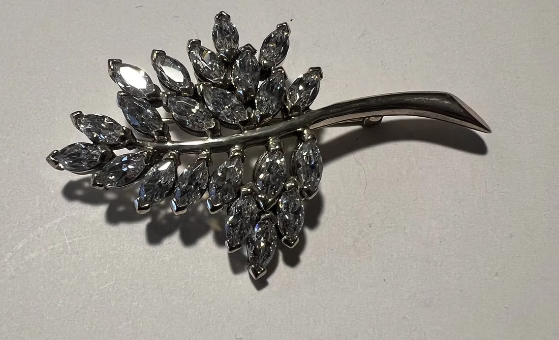 Design & Stones: This is a classic botanical-style brooch shaped like a sprig of leaves or a branch: Designer & Provenance: A beautiful, authentic vintage piece by renowned Hollywood designer Nolan Miller. Known for dressing television royalty and creating high-glamour statements, this piece showcase