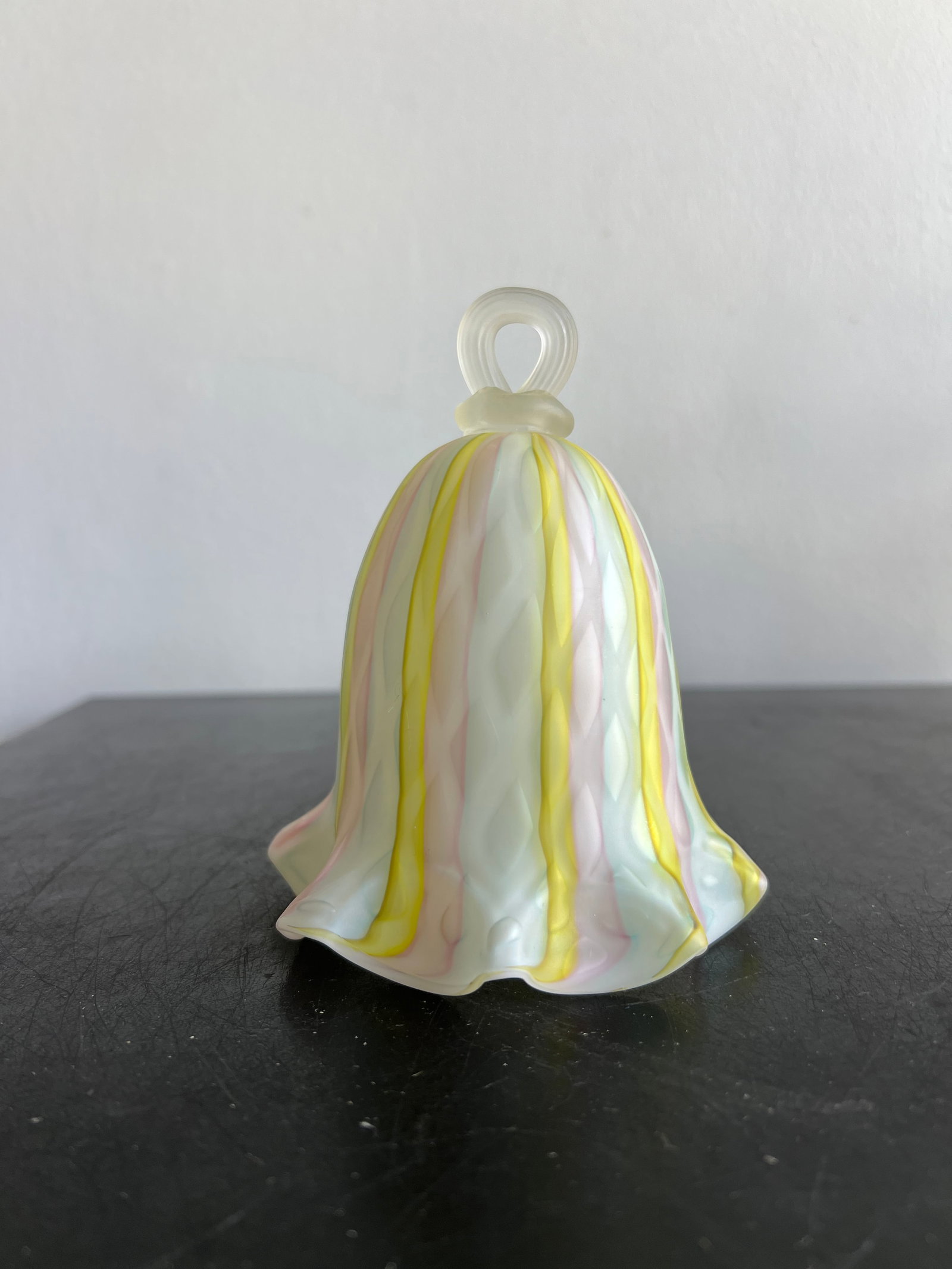 Pastel Striped Art Glass Hand Bell: This piece is a hand-blown studio art glass bell , featuring a classic bell-shaped body with a ruffled, flared rim and a clear glass loop handle at the top. It showcases a soft pastel color palette wi