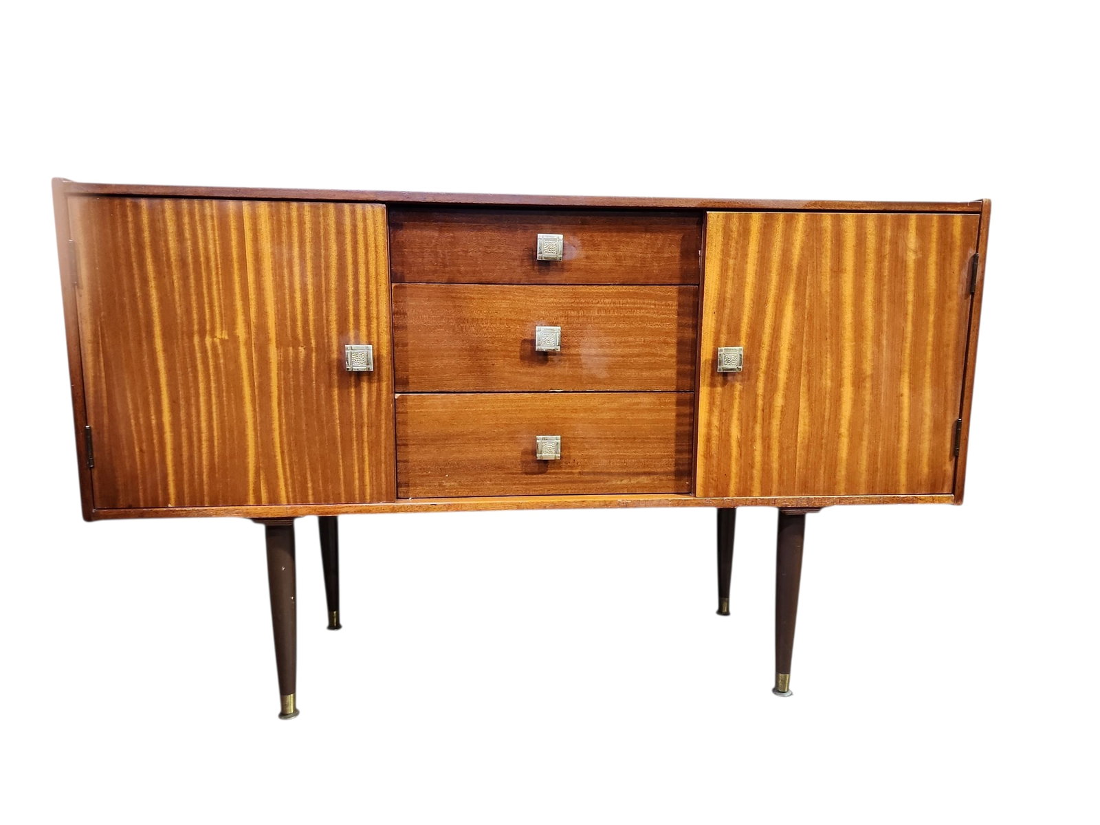 1960s Mid Century Modern Tola Wood Sideboard: Lovely English mid century modern tola wood sideboard in excellent condition. Three central drawers flanked by cabinet to each side, chrome hardware on tipped legs.No makers stamp present, likely a Be