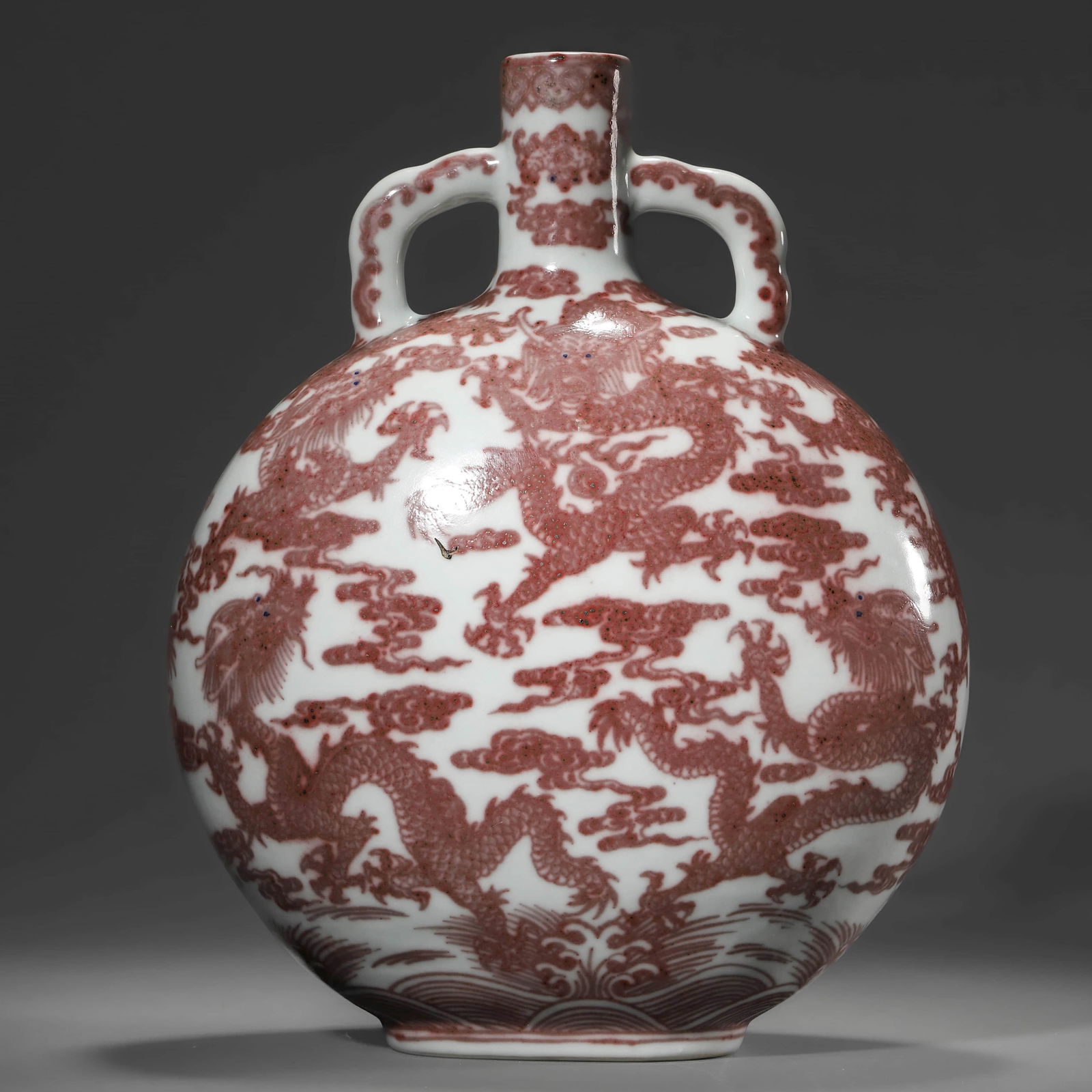 A CHINESE UNDERGLAZE RED MOON FLASK WITH DRAGON MOTIFS.: A CHINESE UNDERGLAZE RED MOON FLASK WITH DRAGON MOTIFS. Dimensions: Height: 11 13/16 in. (30 cm) ALL ITEMS SOLD AS IS, NO RETURNS Condition: Any statement made in any catalogue or otherwis