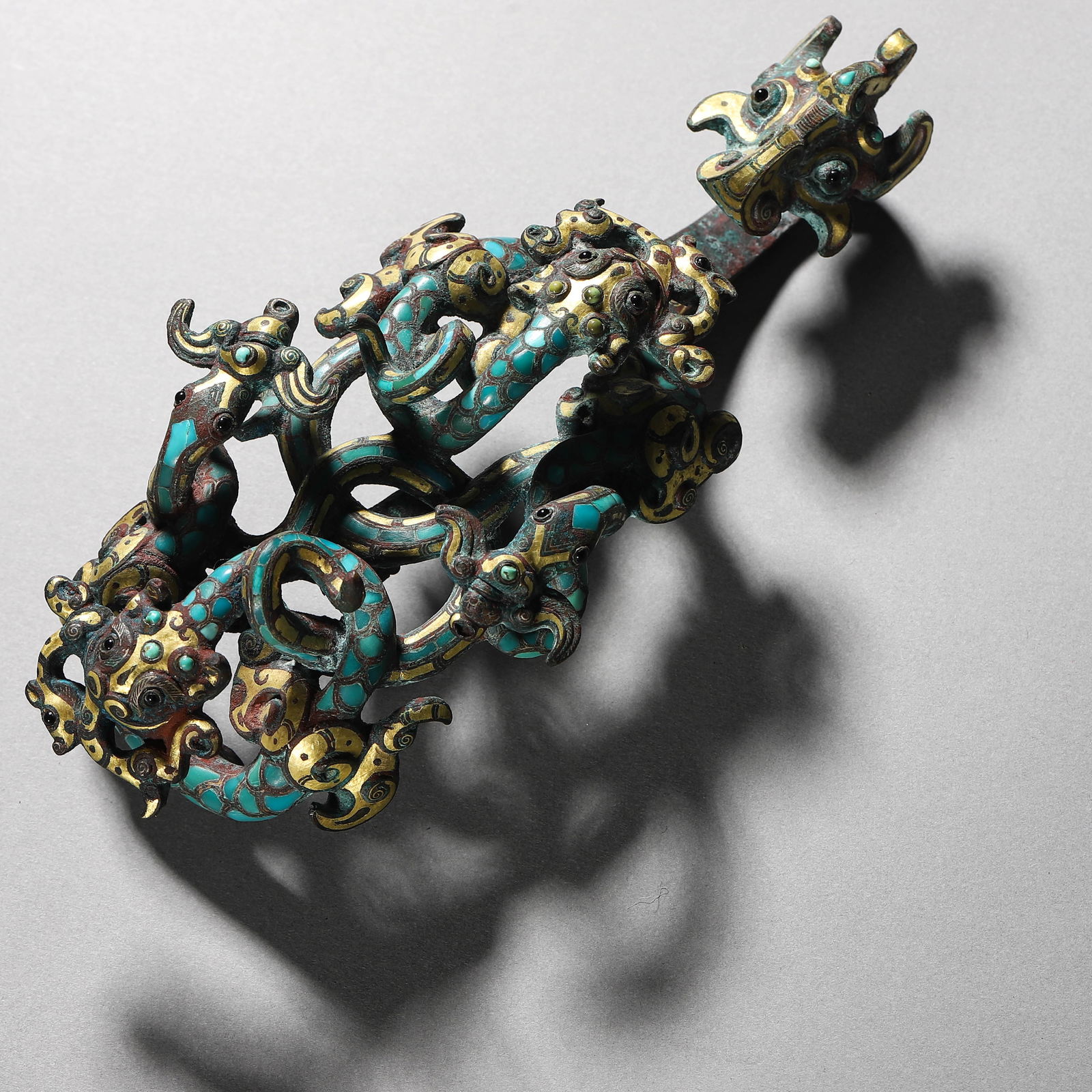 A CHINESE BRONZE AND GOLD DRAGON PATTERN HOOK, EMBELLISHED WITH TURQUOISE.: A CHINESE BRONZE AND GOLD DRAGON PATTERN HOOK, EMBELLISHED WITH TURQUOISE. Dimensions: Length: 7 1/8 in. (18 cm) ALL ITEMS SOLD AS IS, NO RETURNS Condition: Any statement made in any catal