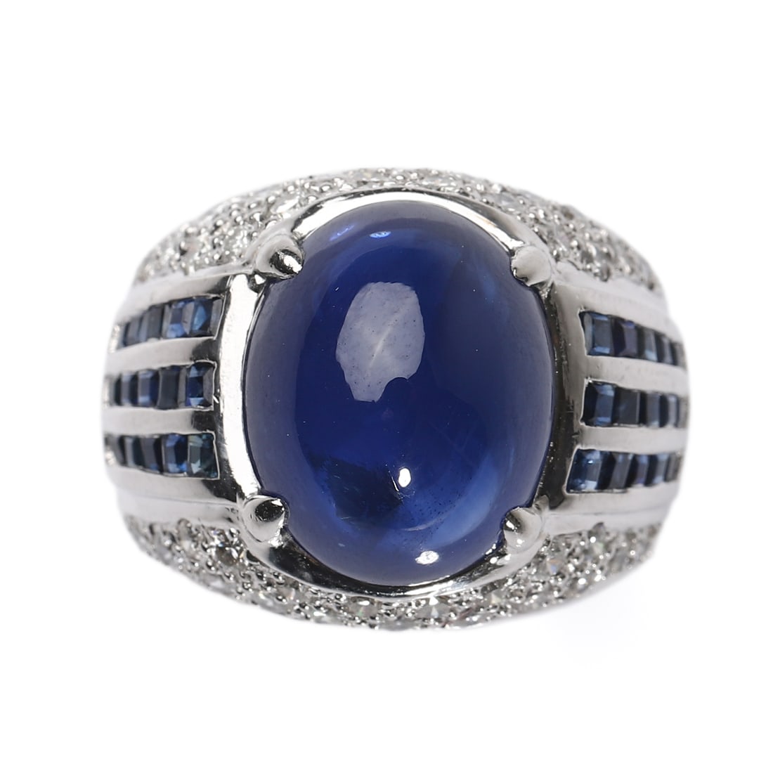 A SAPPHIRE AND DIAMOND RING: Set with an oval cabochon-cut sapphire measuring approximately 14.6 × 11.9 mm, within a pavé-set diamond surround, accented by channel-set calibré-cut sapphires on the shoulders, mounted in 18K whi