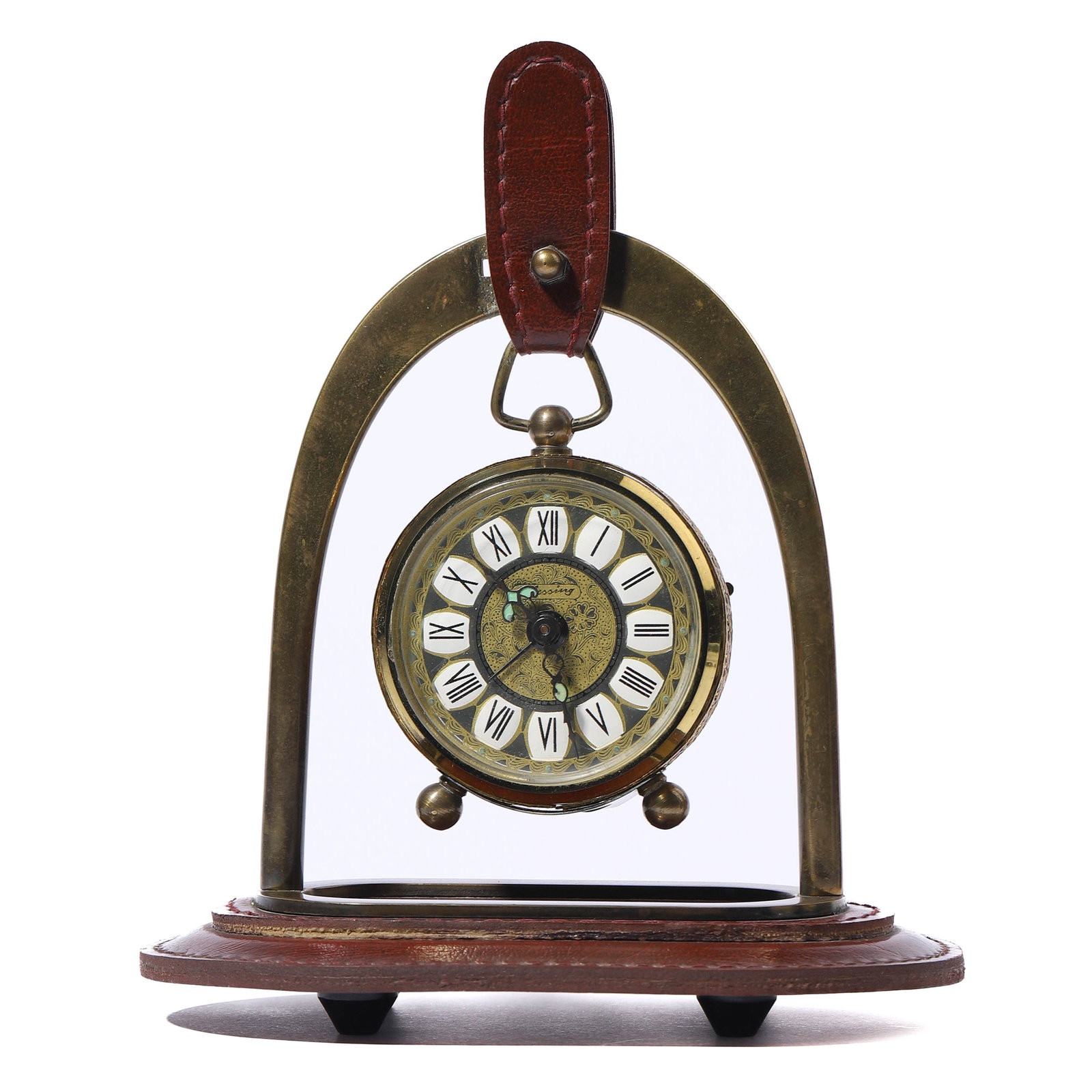 VINTAGE WEST GERMAN BRASS HANGING TABLE CLOCK: dial diameter: 2 5/16 in (5.9 cm); total height: 6 11/16 in (17 cm) A beautifully crafted vintage brass clock with a unique hanging design, supported by a leather strap on an arched brass frame mounte