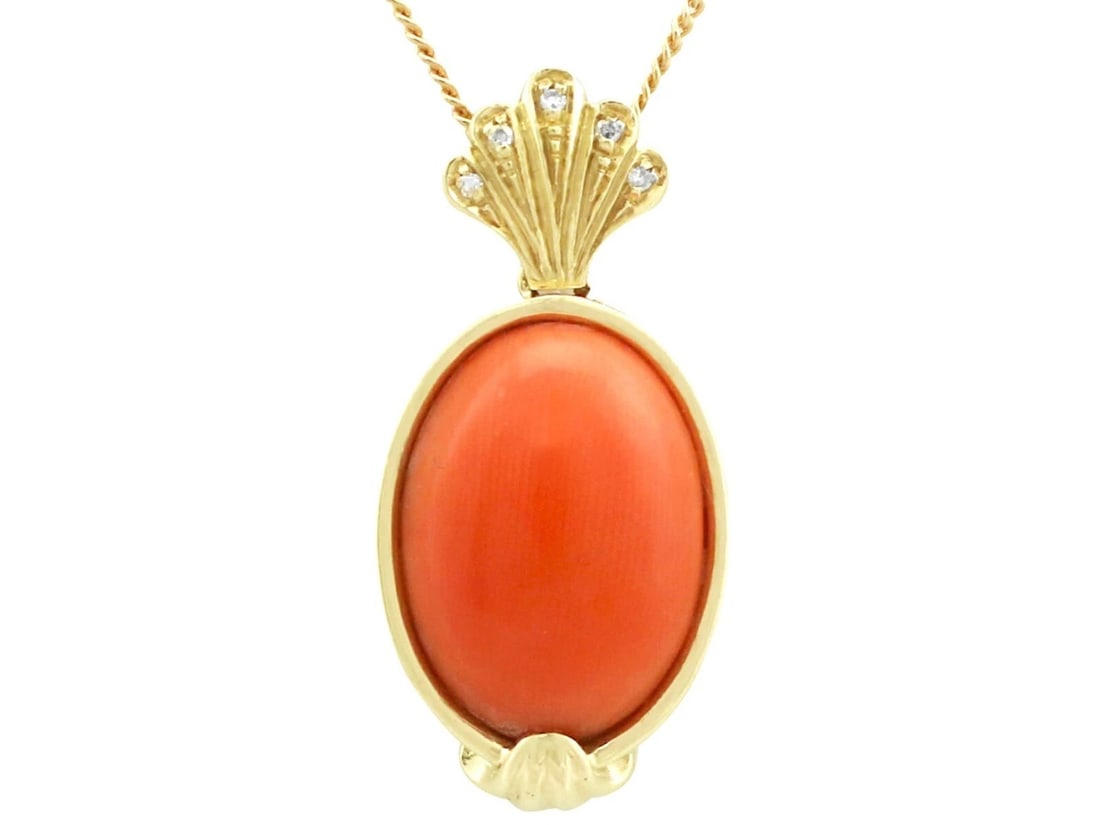GOLD-TONE CORAL-COLOR OVAL PENDANT BROOCH: GOLD-TONE CORAL-COLOR OVAL PENDANT BROOCH Description: An oval gold-tone pendant-brooch centered by a smooth coral-color cabochon, framed by a sculptural textured border and fitted for both pendant an